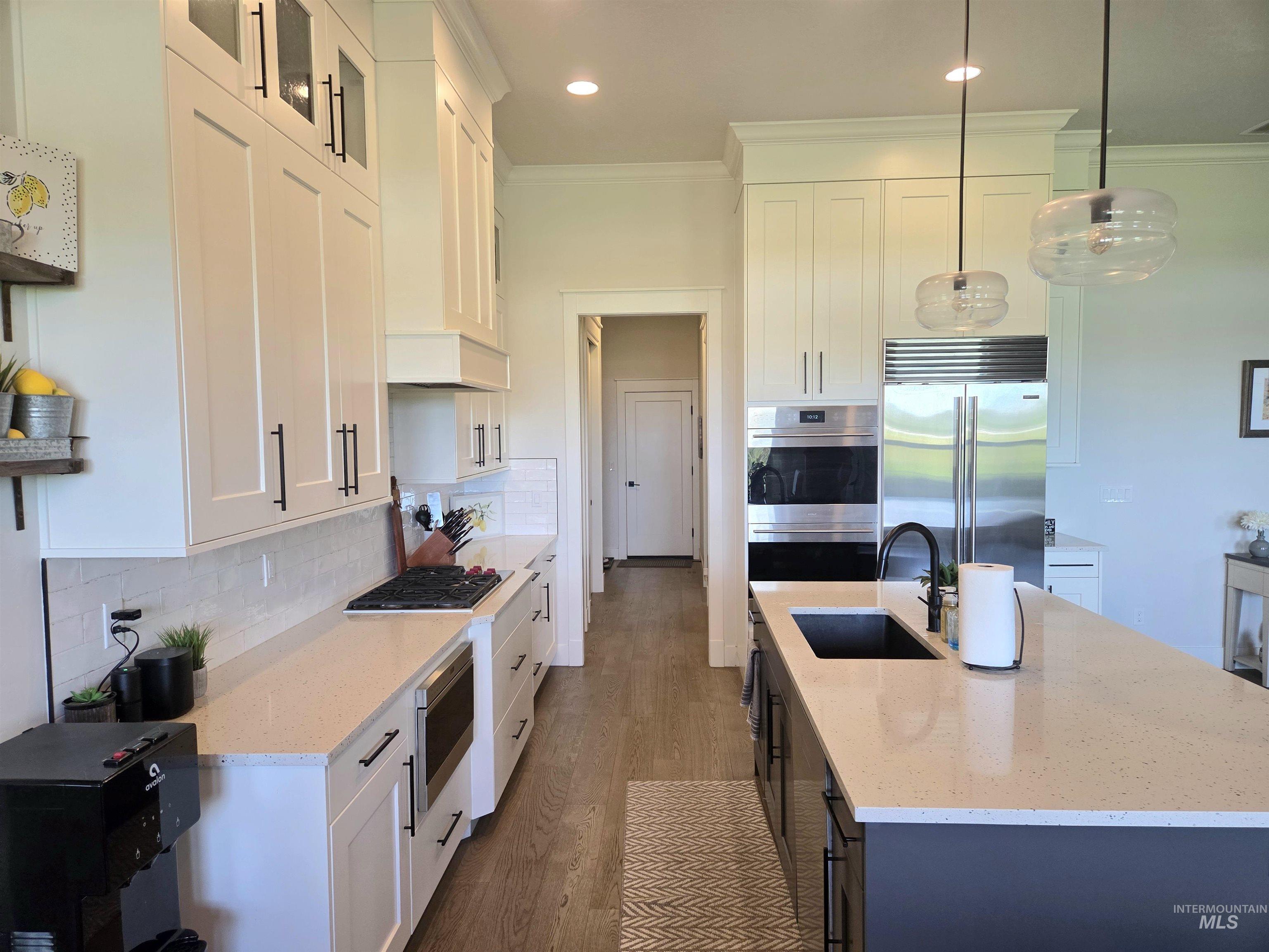 Kitchen with ornamental molding, a kitchen island with sink, decorative backsplash, SubZero and Wolf appliances, and wood finished floors