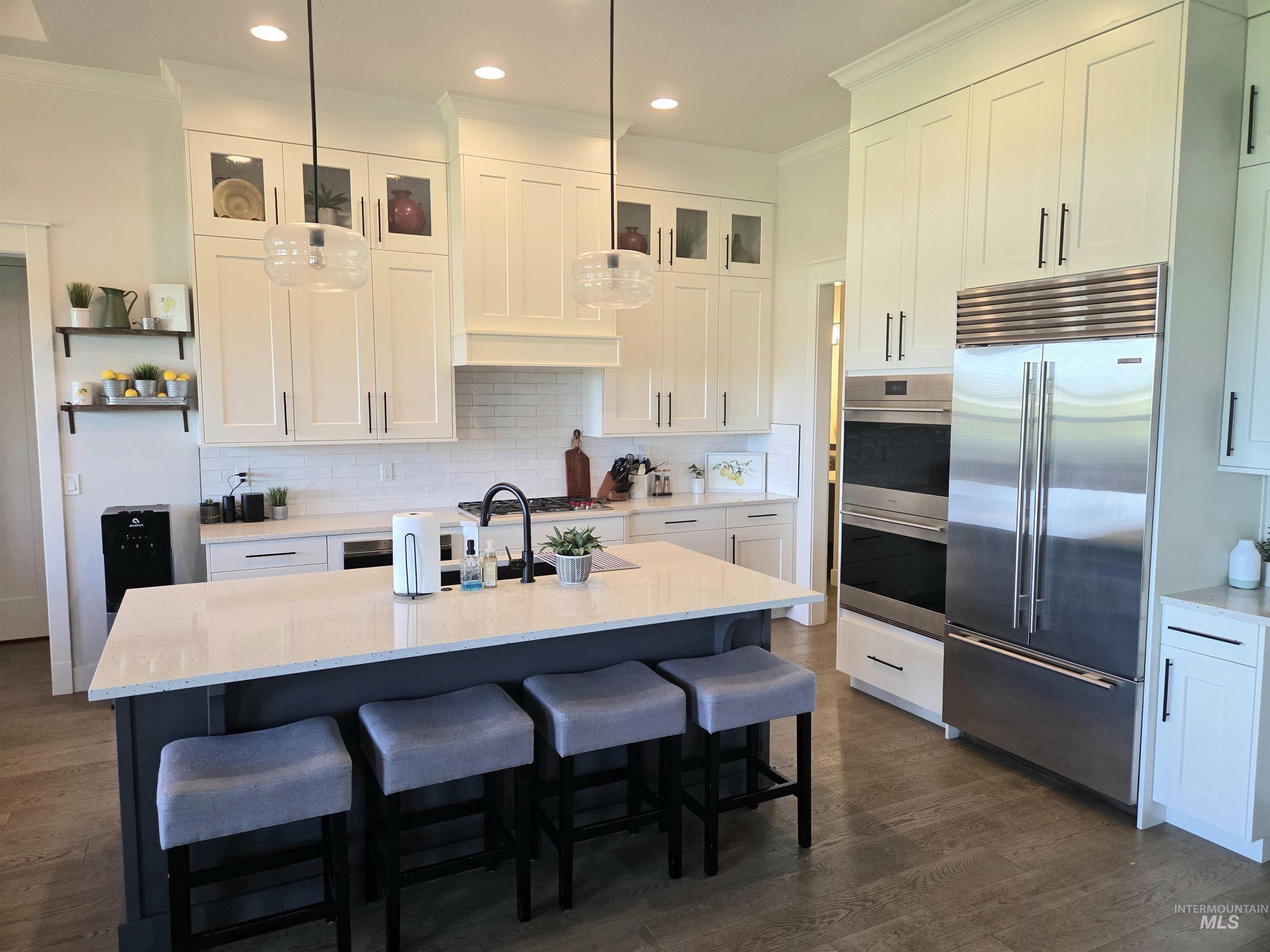 Kitchen featuring crown molding, SubZero and Wolf appliances with stainless steel finishes, dark wood-type flooring, tasteful backsplash, and a kitchen bar with quartz countertops