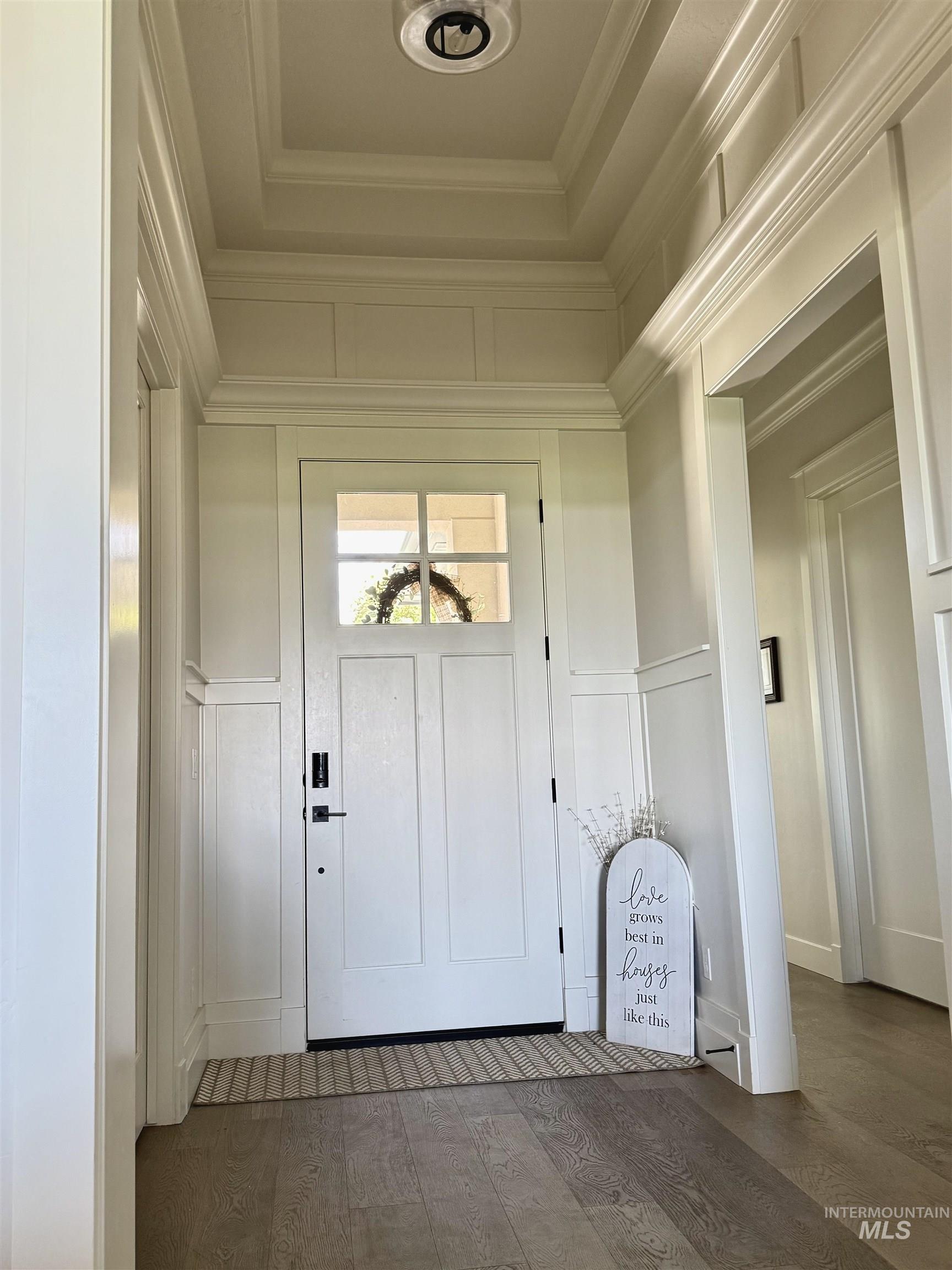 Entryway with a decorative wall, hardwood / wood-style floors, a raised ceiling, and ornamental molding