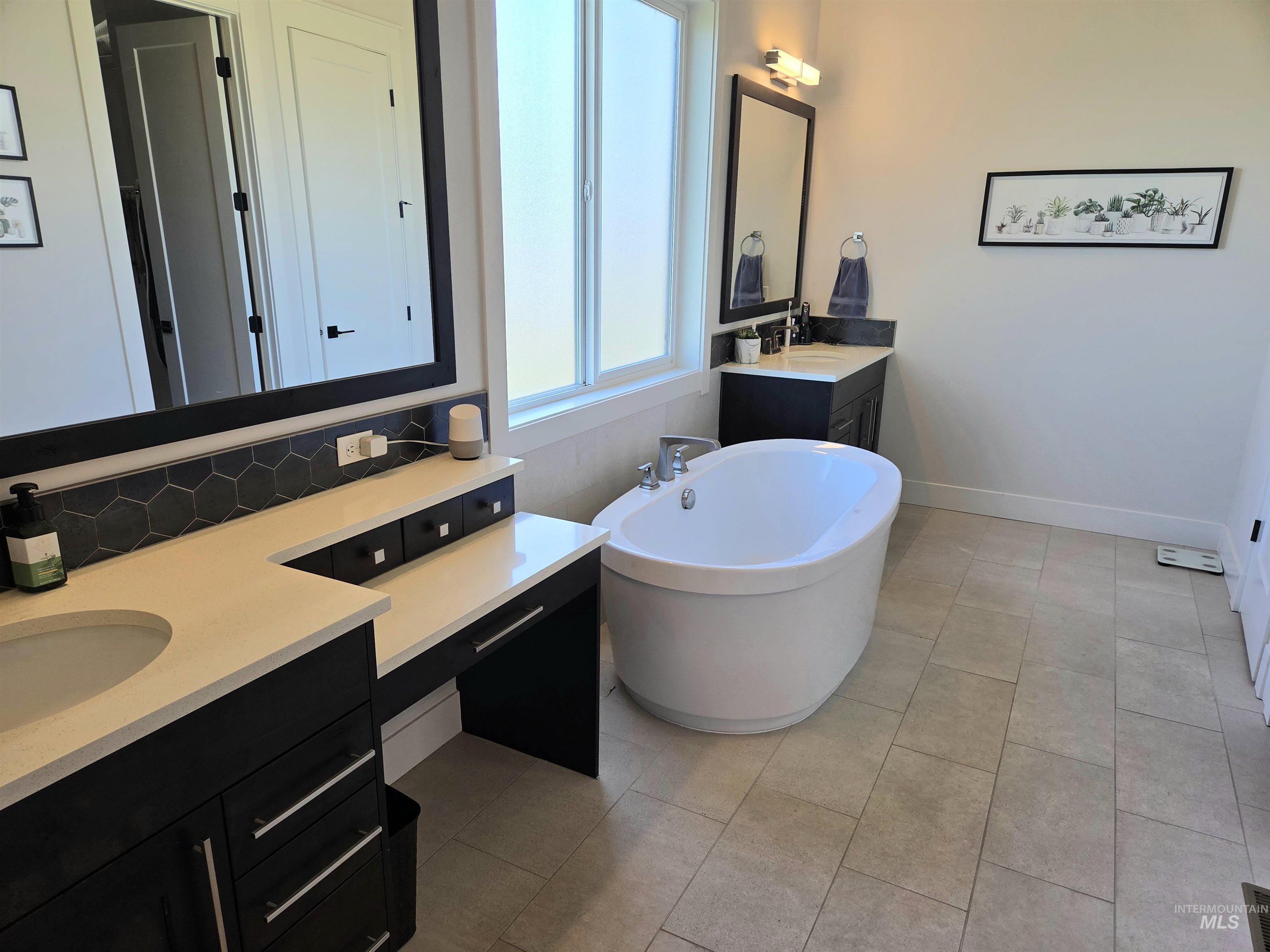 Bathroom with a freestanding bath, two vanities, tile patterned flooring, and backsplash