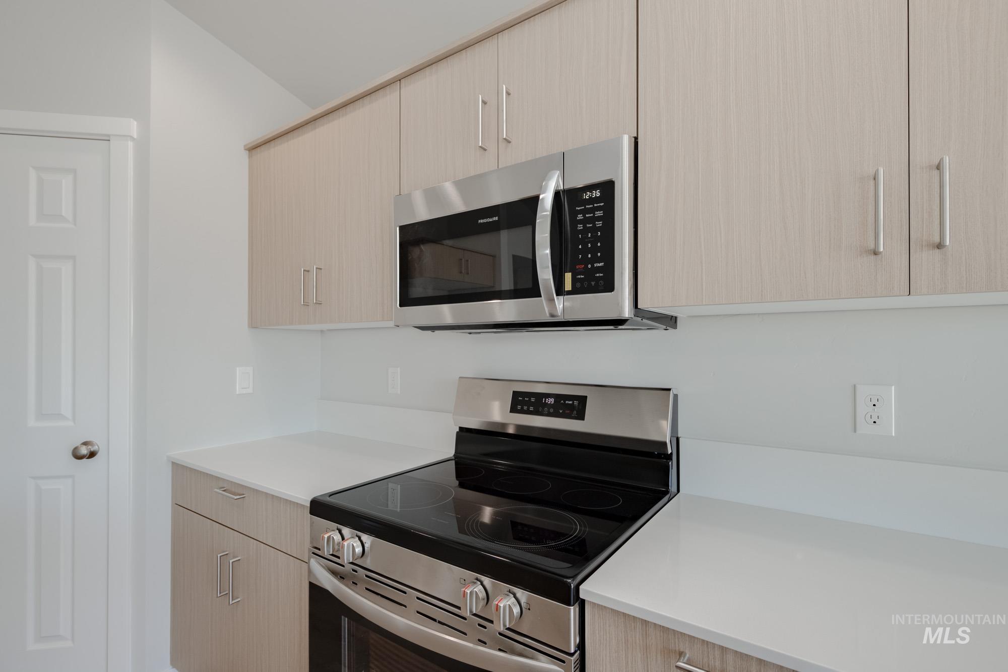 Kitchen featuring appliances with stainless steel finishes, light brown cabinets, modern cabinets, and light stone counters