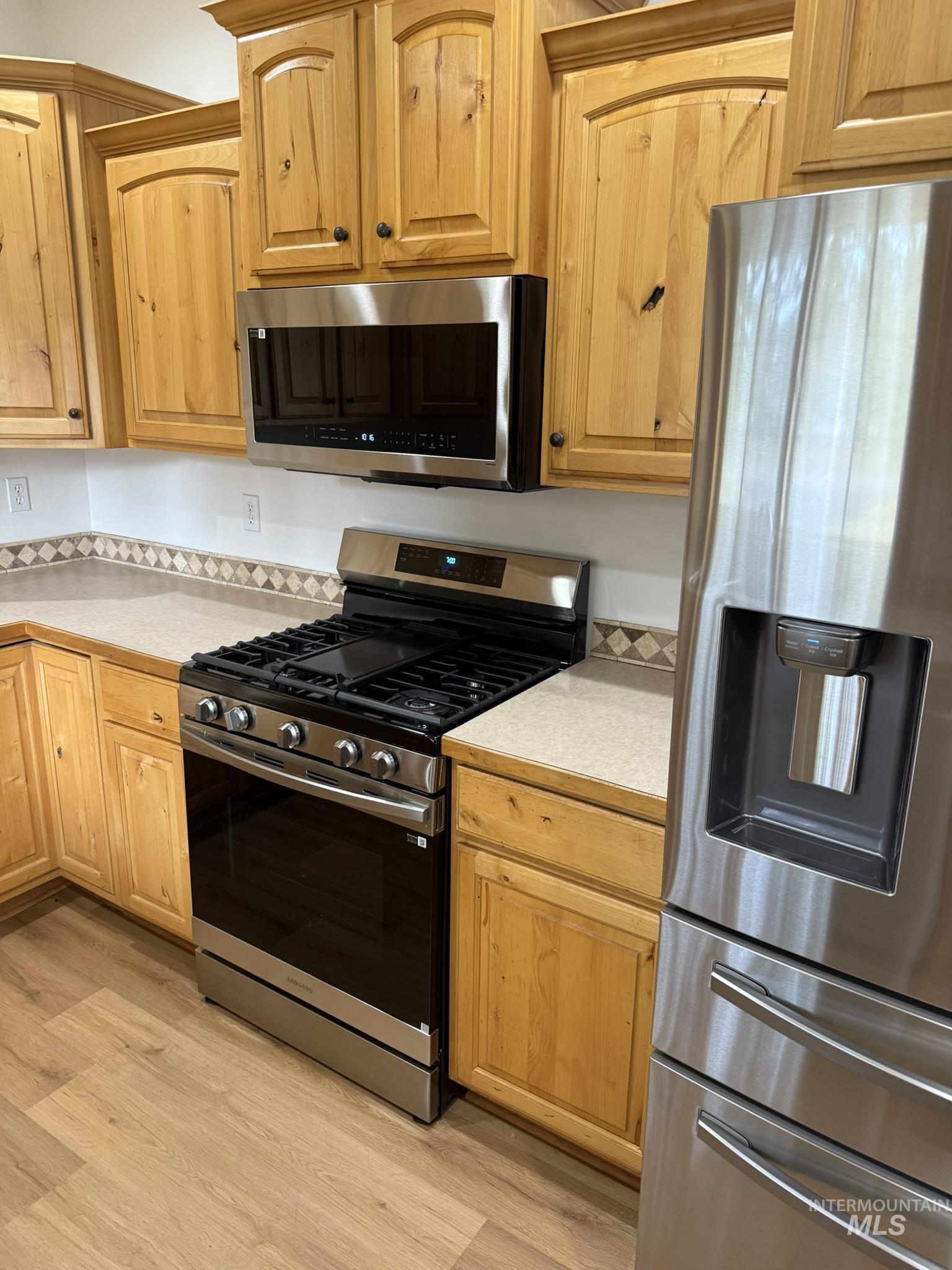 Kitchen with appliances with stainless steel finishes, light countertops, light wood-type flooring, and light brown cabinetry