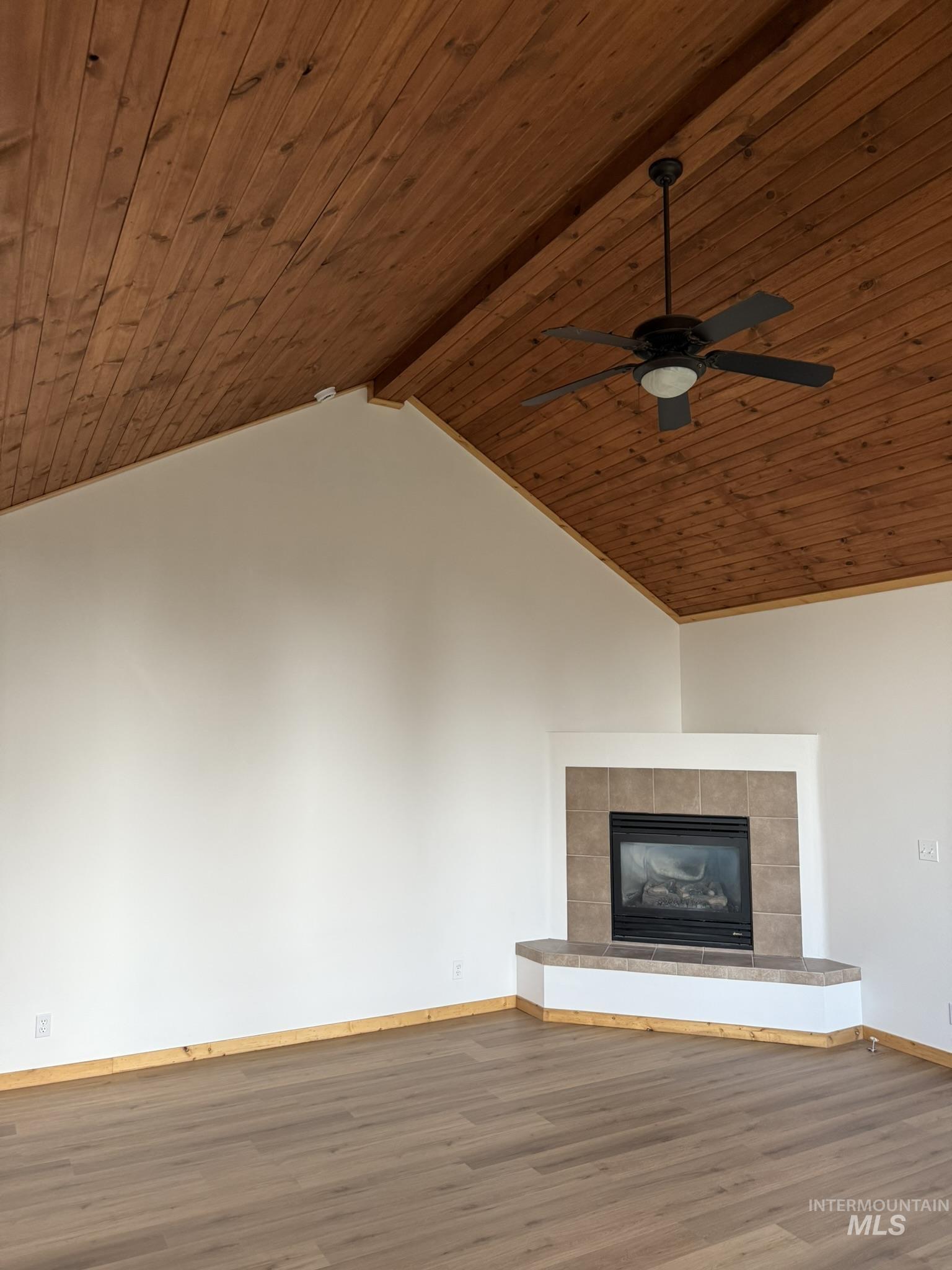 Unfurnished living room with wood finished floors, a tiled fireplace, wooden ceiling, and ceiling fan