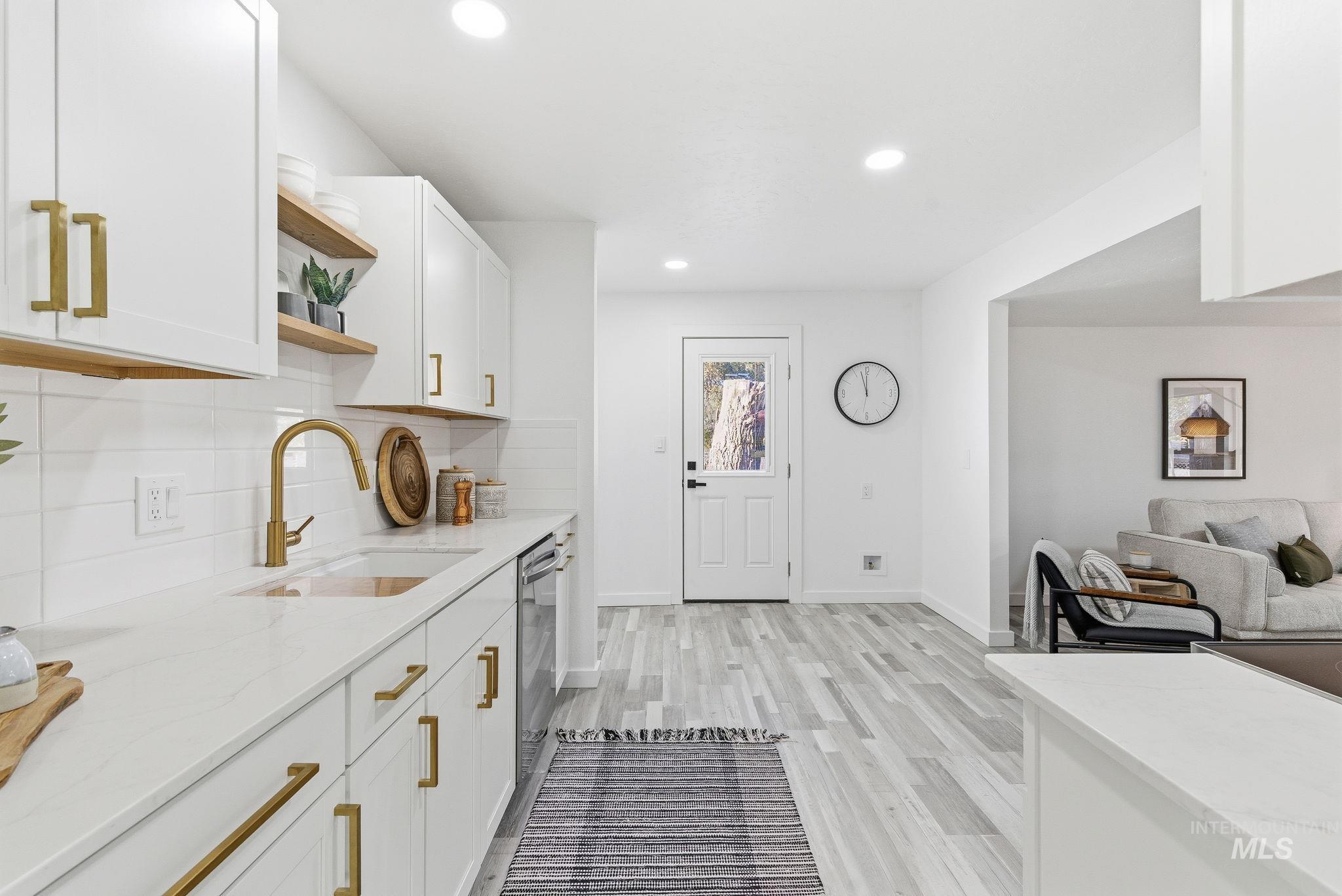 Kitchen with open shelves, backsplash, light stone countertops, white cabinets, and light wood-style floors