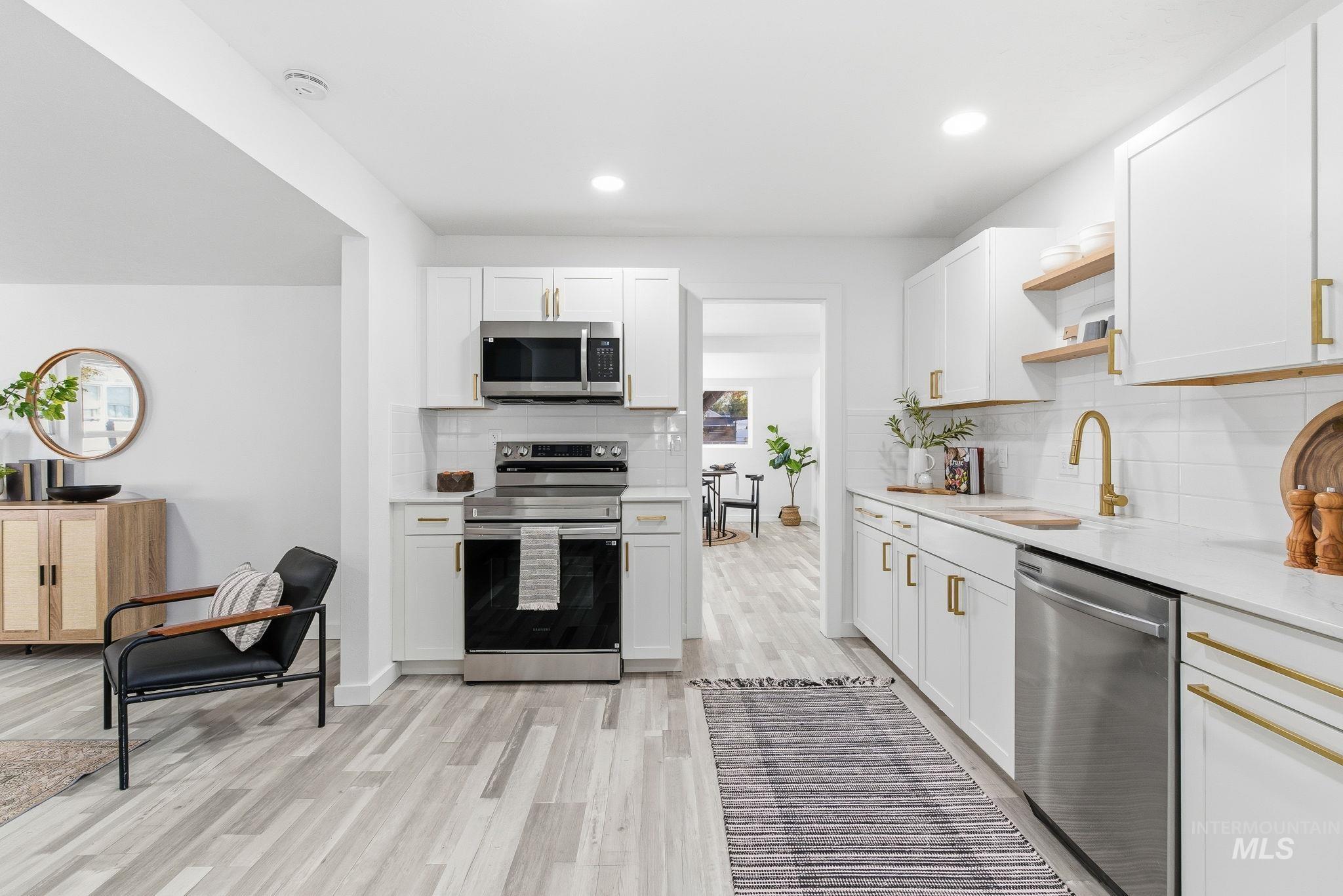 Kitchen with stainless steel appliances, tasteful backsplash, white cabinets, light wood-style floors, and open shelves
