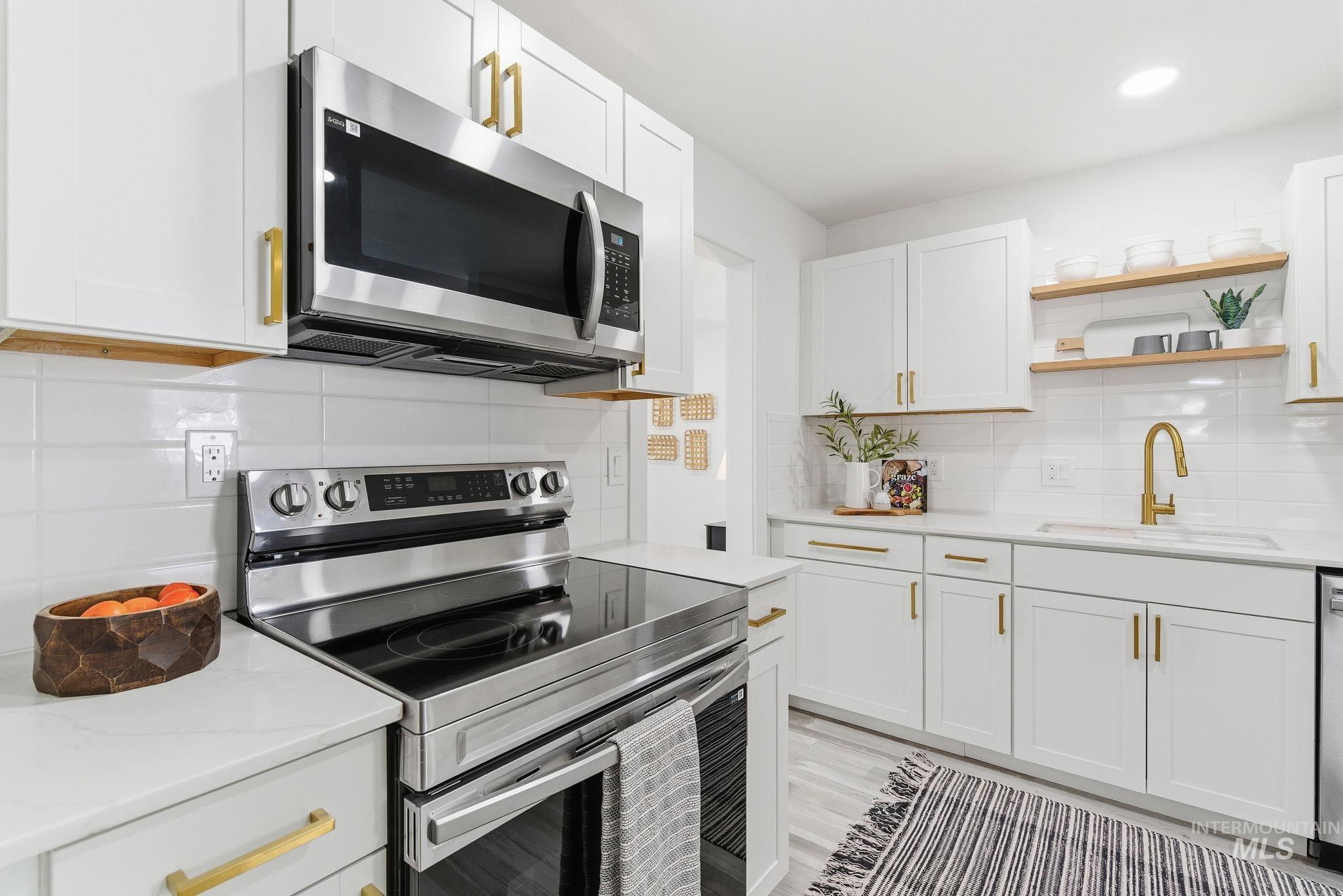 Kitchen featuring appliances with stainless steel finishes, tasteful backsplash, open shelves, white cabinetry, and light stone counters