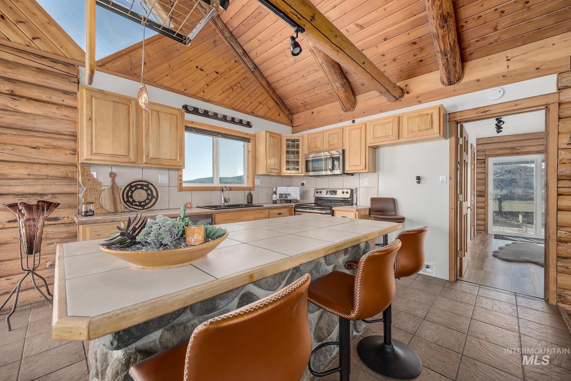 Kitchen featuring log walls, a high wooden beamed ceiling, a breakfast bar, light wood finish cabinetry, and plenty of natural light