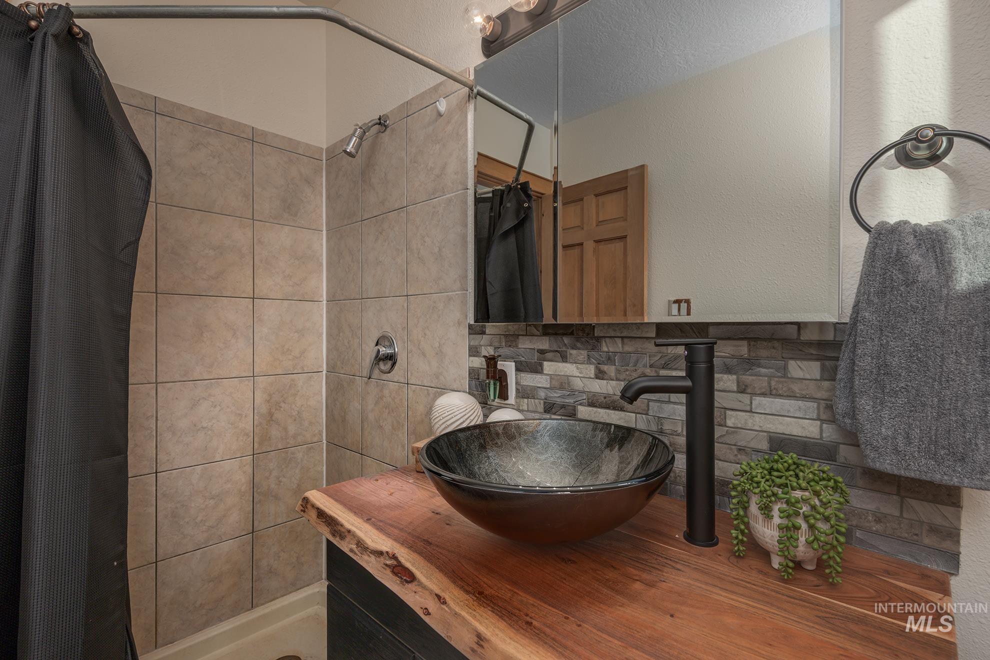 Bathroom with a shower stall, vanity, a textured wall, and tasteful backsplash