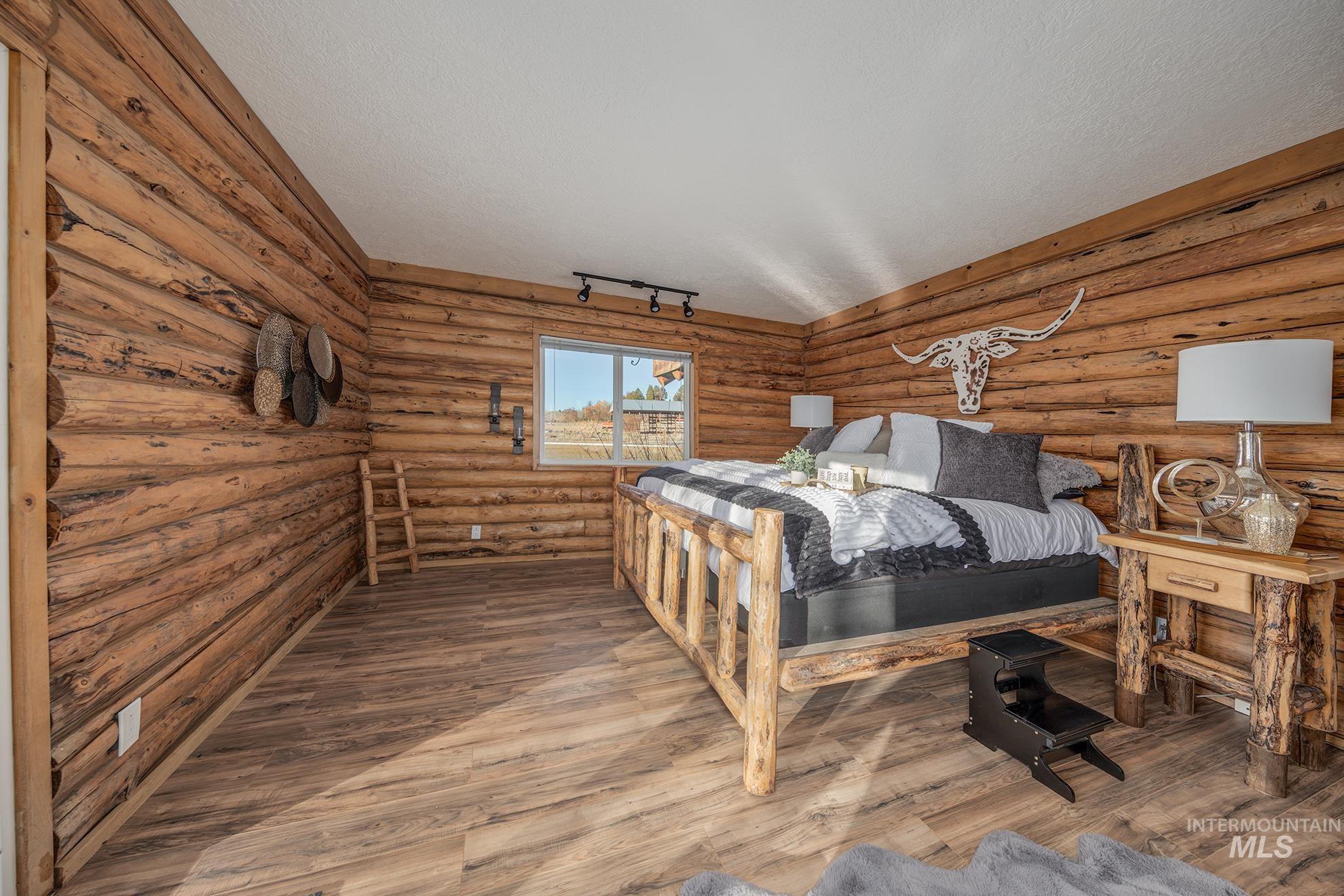 Bedroom with log walls, a textured ceiling, wood-type flooring, and rail lighting