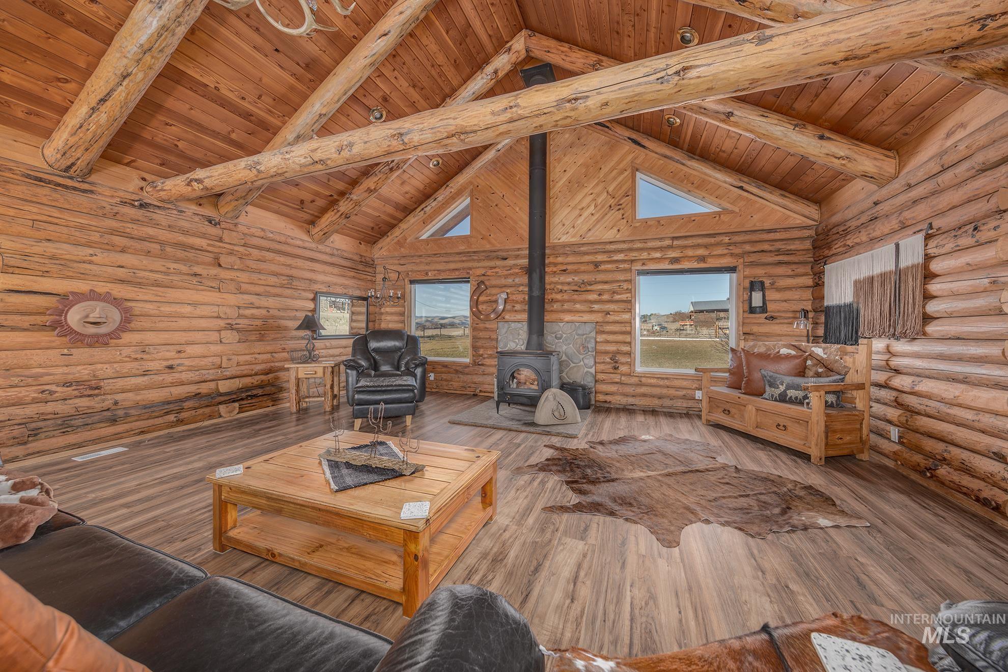 Living area with rustic walls, a wood stove, a high wooden beamed ceiling, and hardwood / wood-style flooring