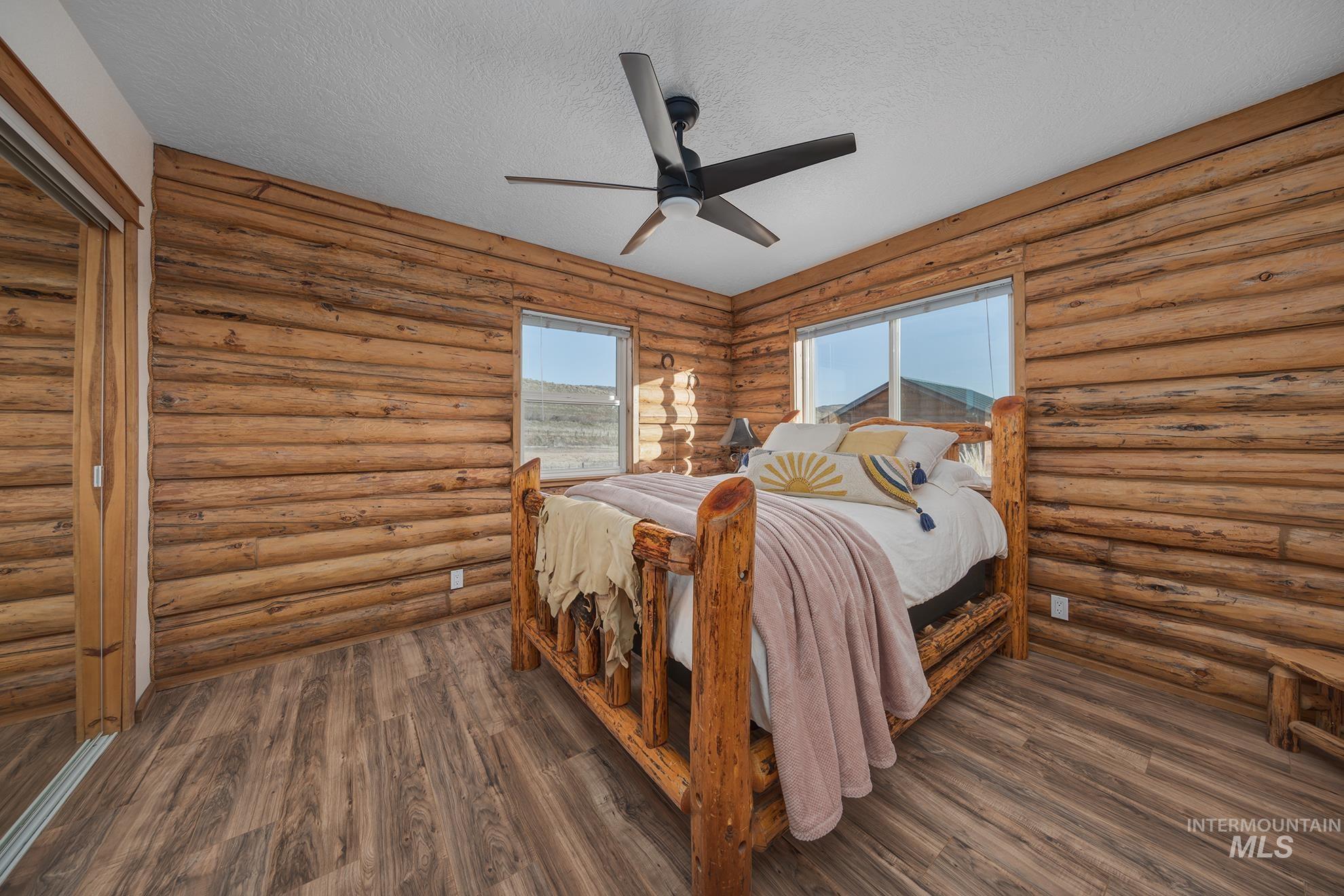 Bedroom with a textured ceiling, rustic walls, a ceiling fan, a closet, and dark wood-type flooring