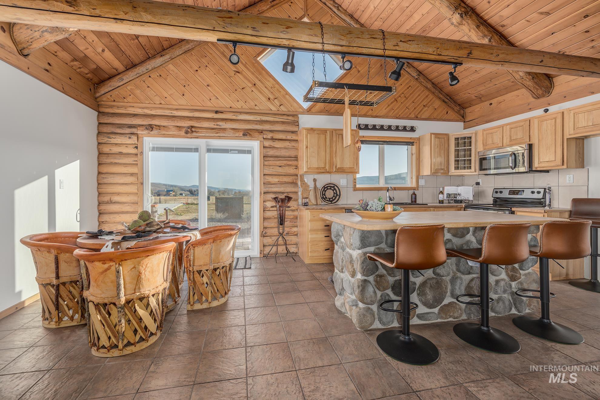 Kitchen featuring a high wooden beamed ceiling, track lighting, glass fronted cabinets, light wood finish cabinets, and rustic walls