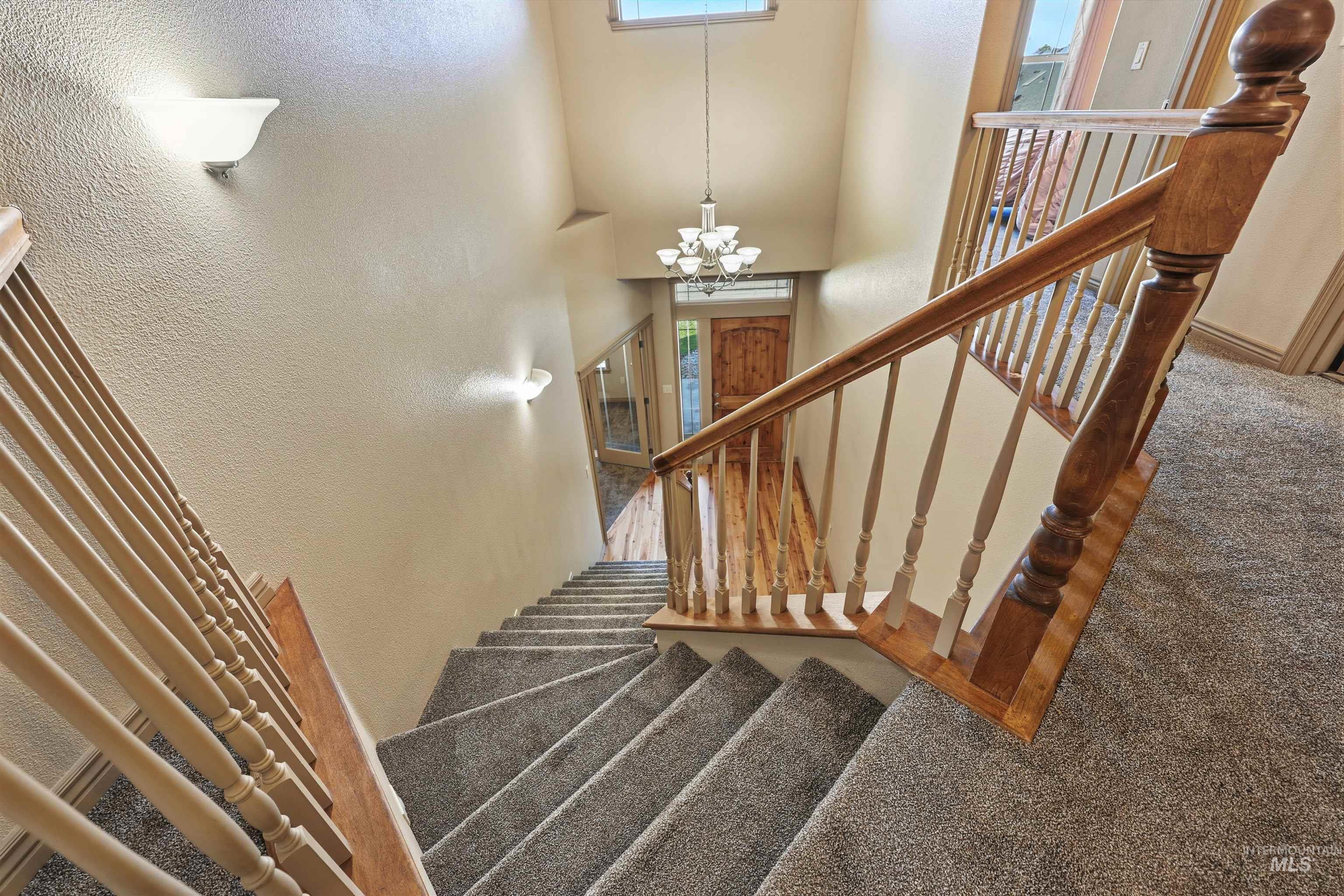 Stairway featuring a textured wall, carpet flooring, a chandelier, and a high ceiling