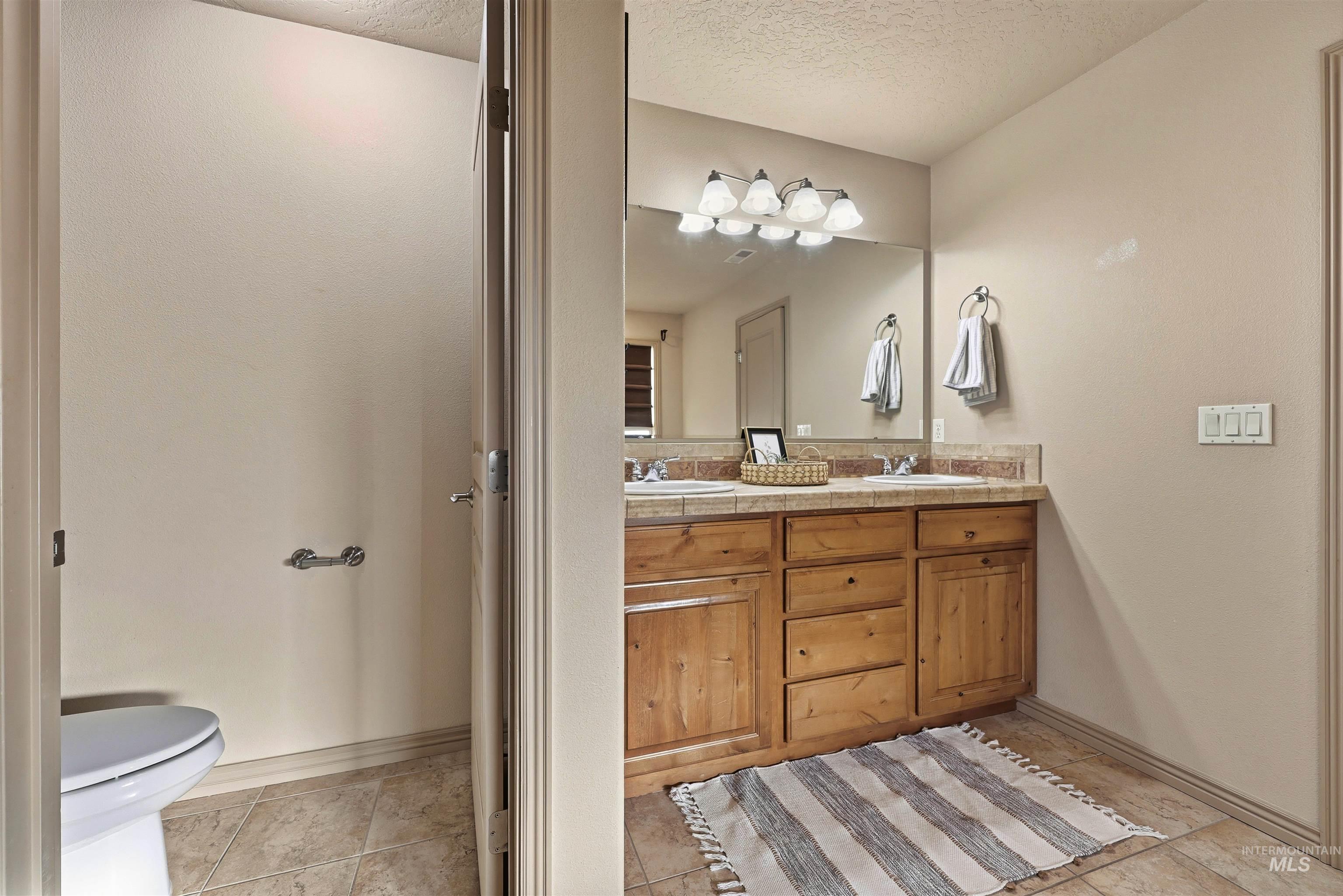 Full bathroom with double vanity, light tile patterned flooring, and a textured ceiling