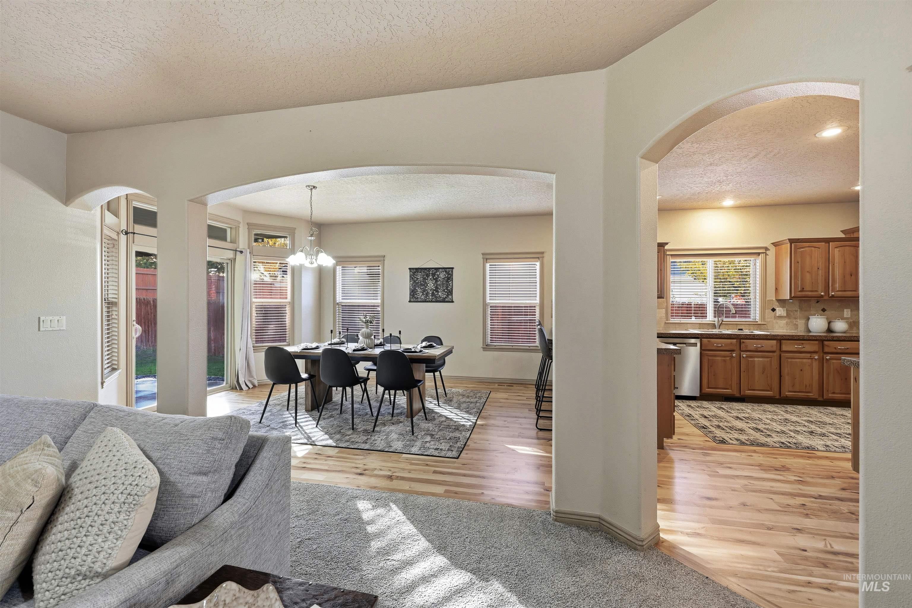 Dining room with a textured ceiling, arched walkways, a chandelier, light wood-style flooring, and recessed lighting