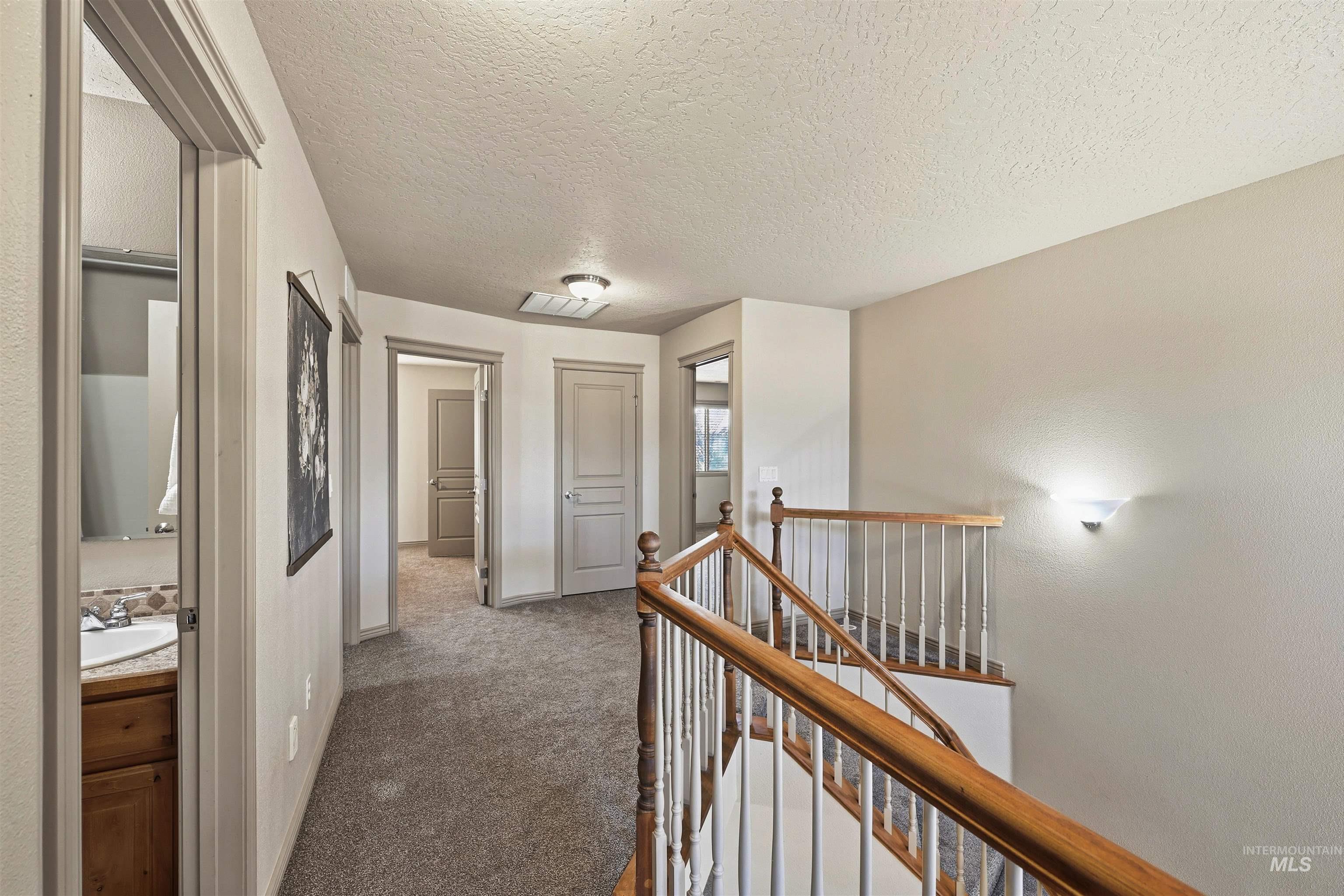Hallway with dark carpet, a textured ceiling, and an upstairs landing