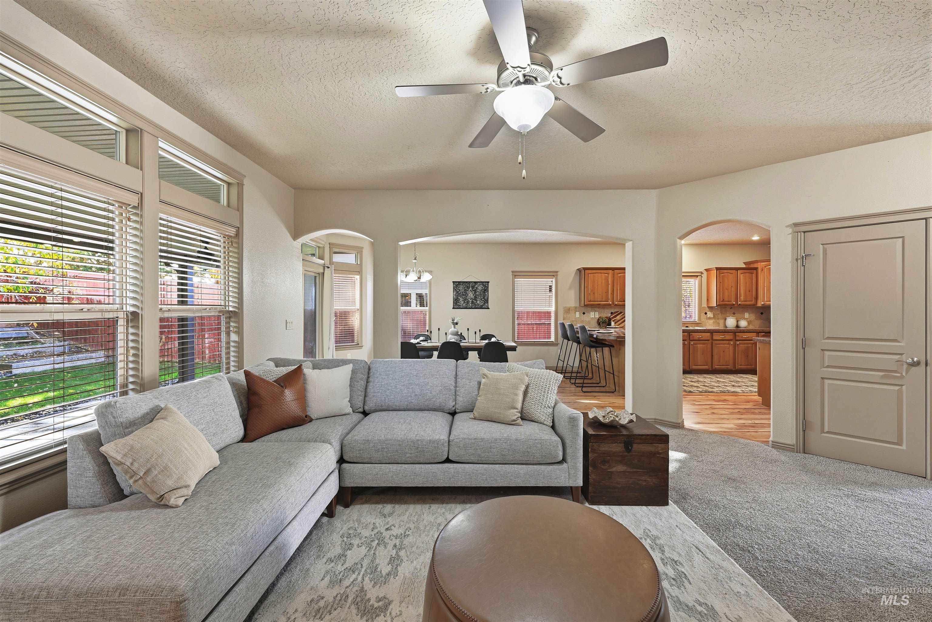 Living area with light colored carpet, arched walkways, a textured ceiling, and ceiling fan