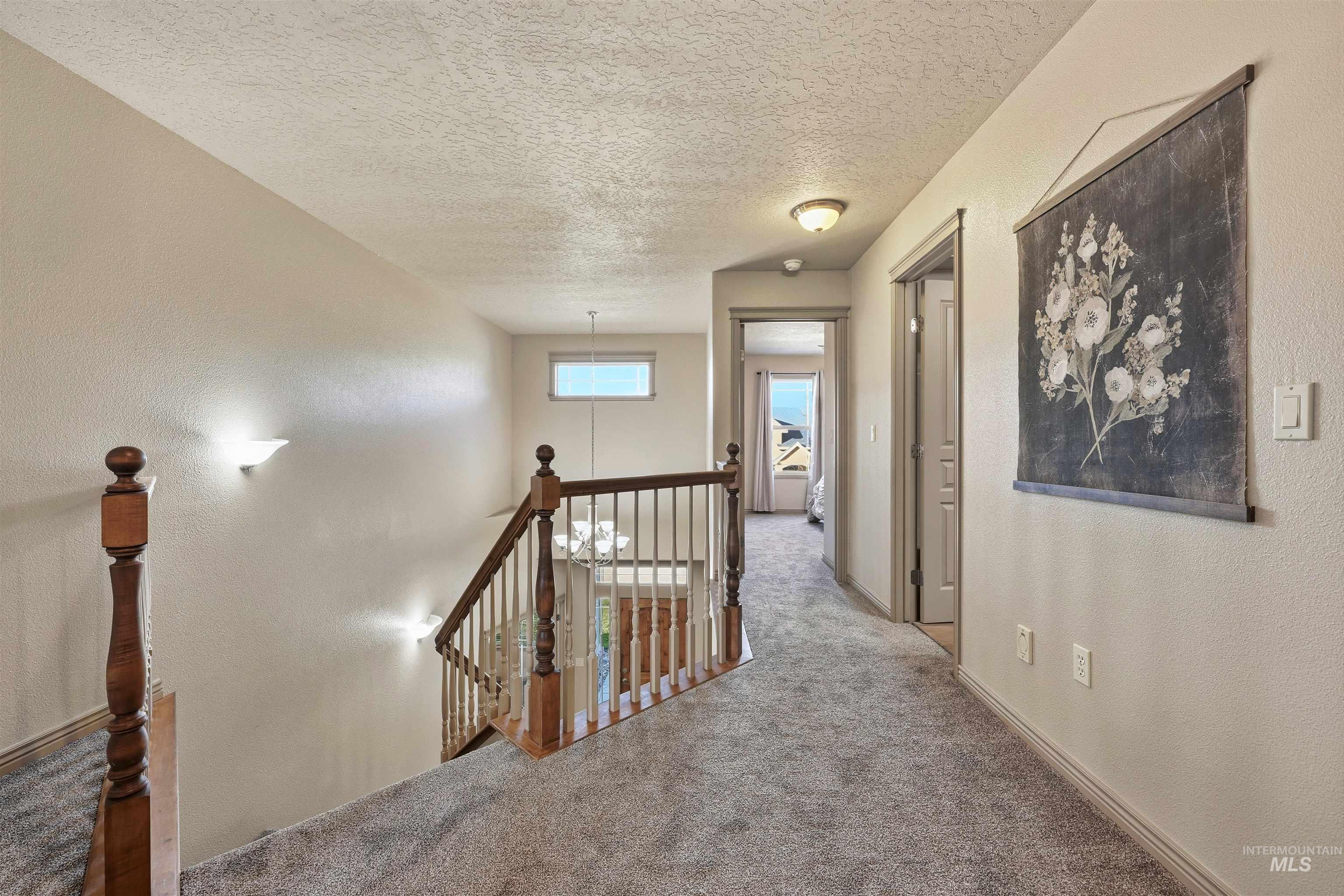 Hallway with a textured wall, an upstairs landing, carpet floors, and a textured ceiling