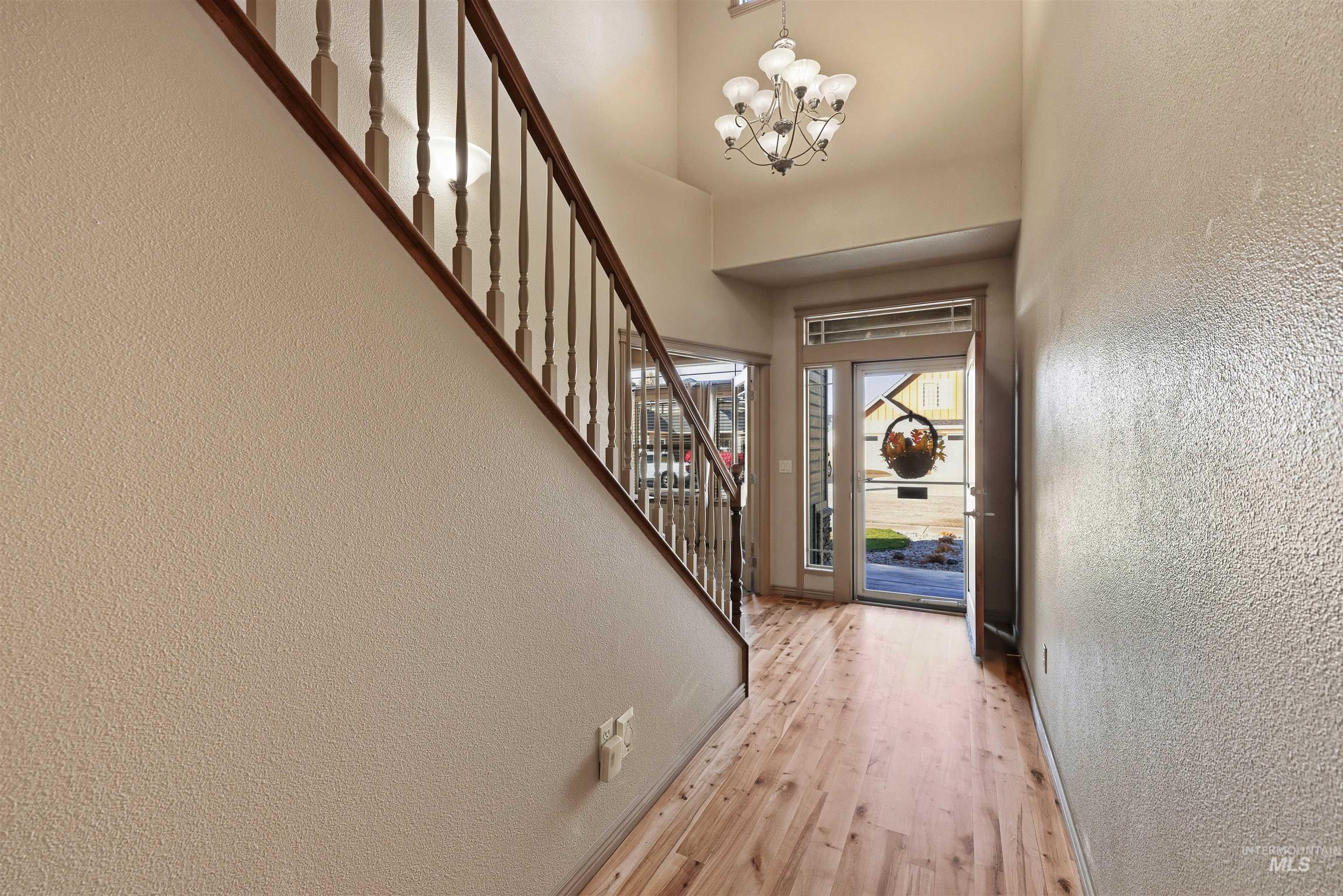 Entryway with a textured wall, light wood-style floors, stairway, and a chandelier