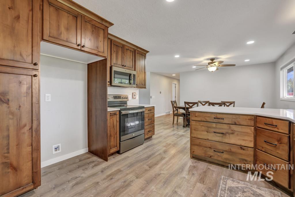 Kitchen with appliances with stainless steel finishes, brown cabinetry, light countertops, recessed lighting, and light wood-style floors