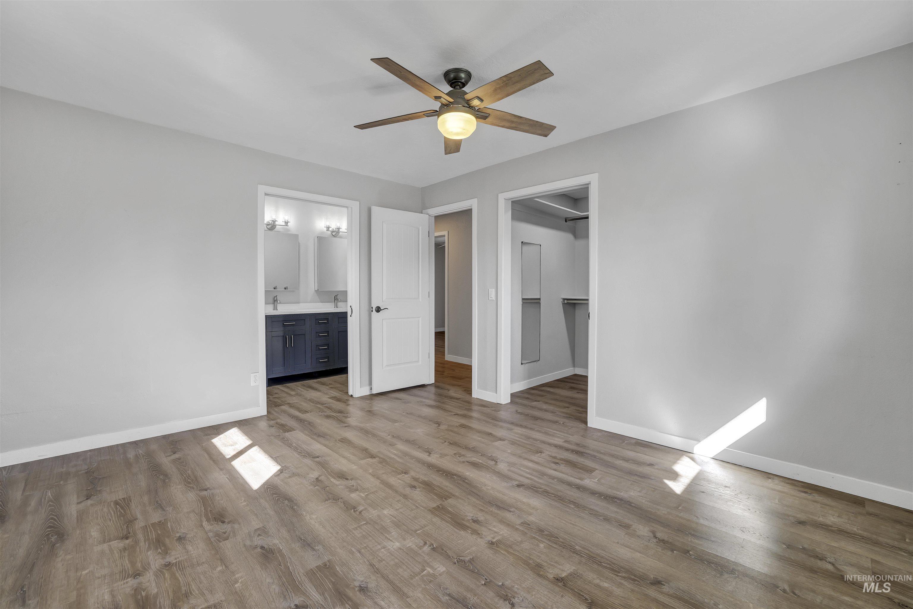 Unfurnished bedroom with light wood finished floors, a spacious closet, ceiling fan, and ensuite bath