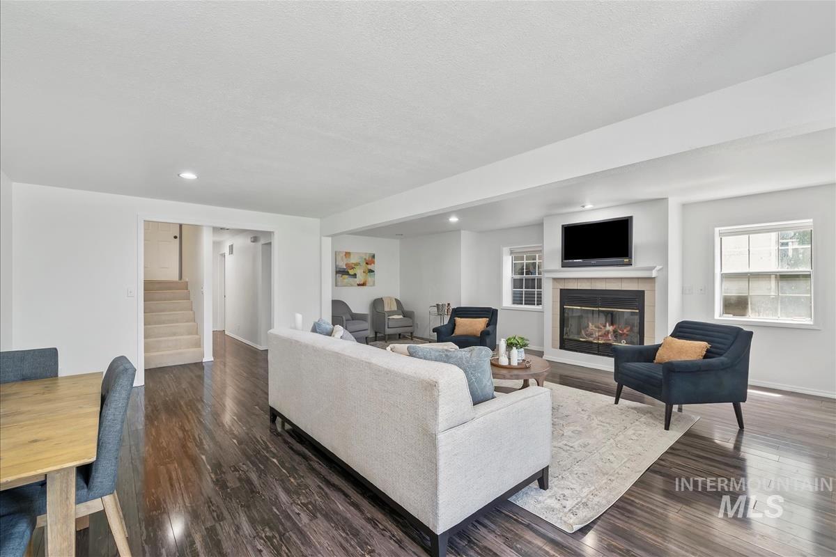 Living room with stairs, recessed lighting, a tiled fireplace, dark wood-style flooring, and a textured ceiling