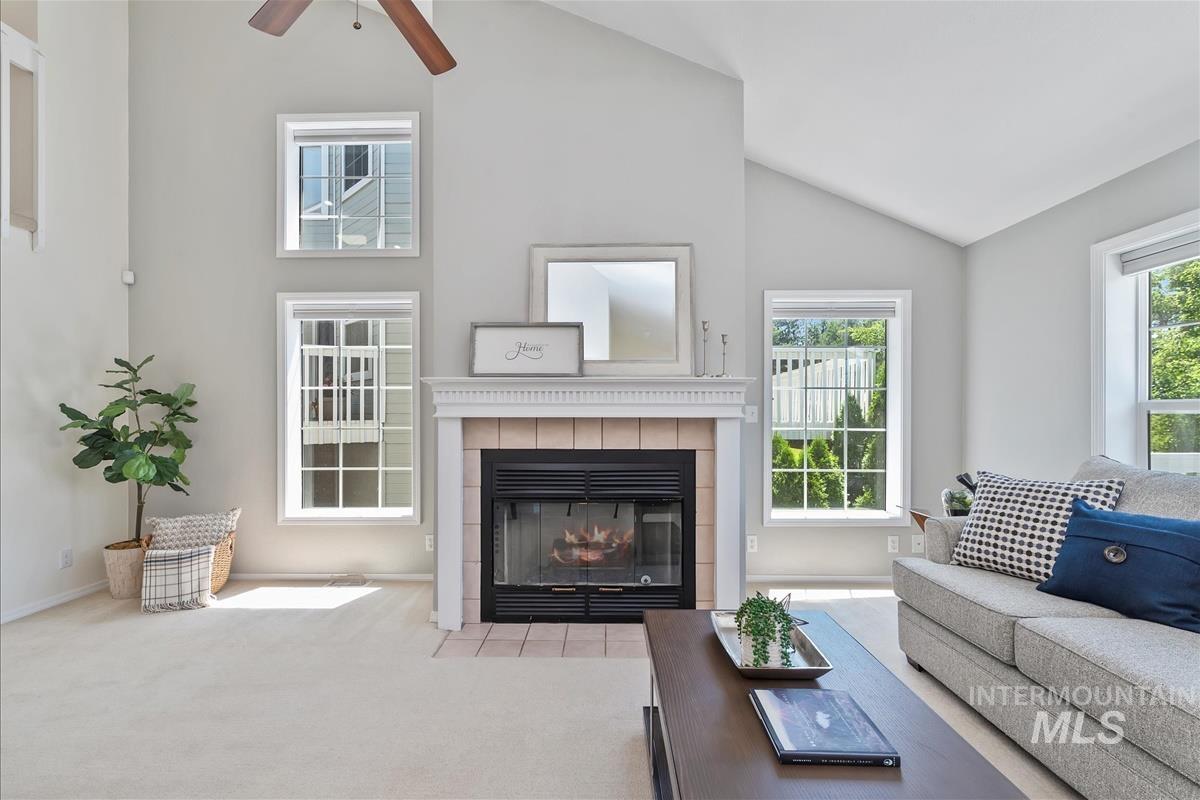 Carpeted living room with lofted ceiling, a ceiling fan, and a fireplace