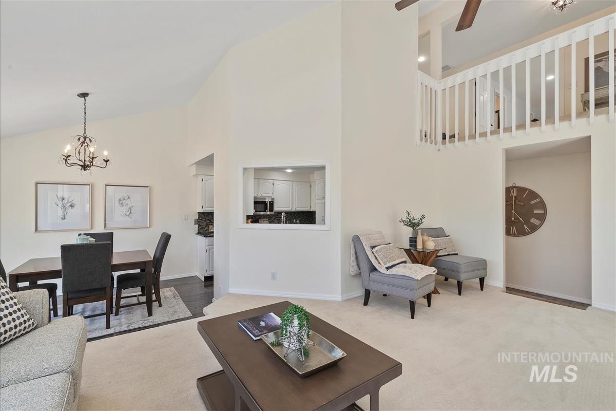 Living area featuring carpet floors, a chandelier, high vaulted ceiling, and a ceiling fan