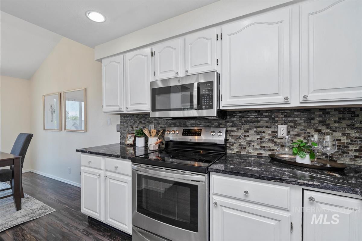 Kitchen with appliances with stainless steel finishes, backsplash, white cabinets, lofted ceiling, and recessed lighting