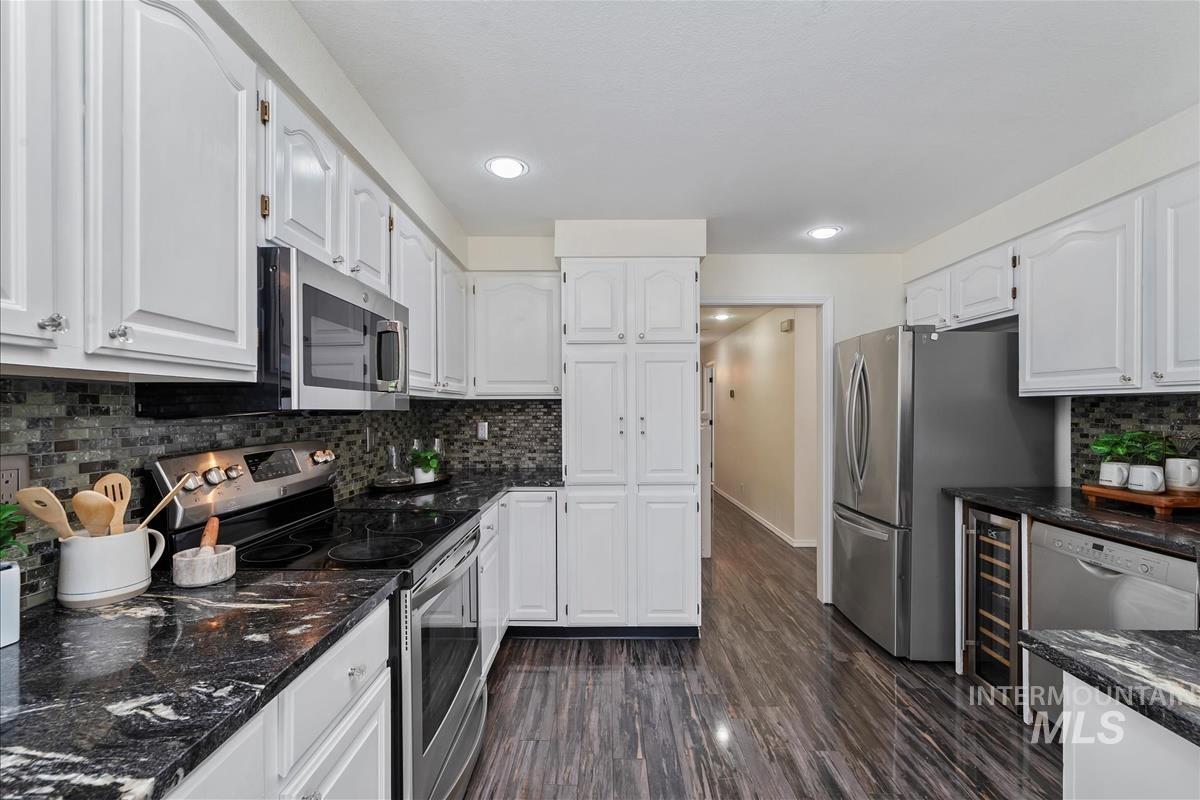 Kitchen with appliances with stainless steel finishes, white cabinetry, wine cooler, and recessed lighting