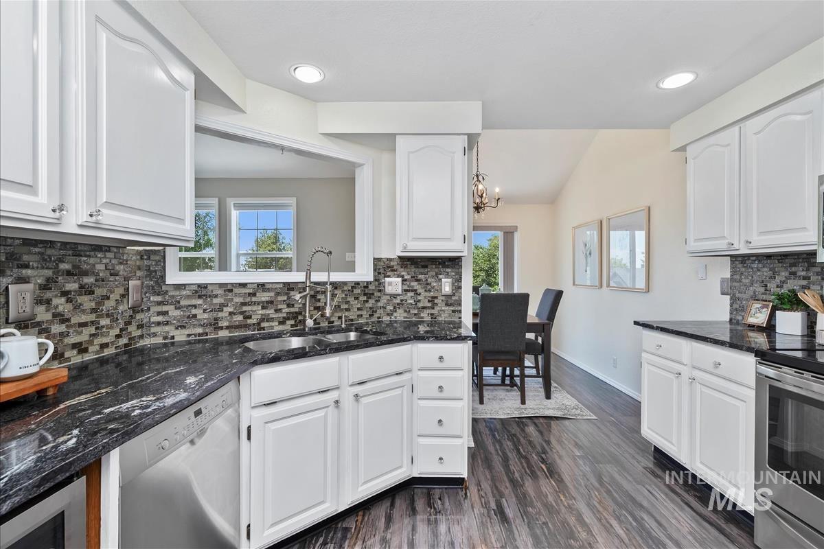 Kitchen with appliances with stainless steel finishes, healthy amount of natural light, tasteful backsplash, white cabinets, and lofted ceiling
