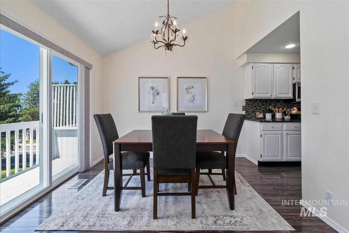 Dining room featuring healthy amount of natural light, a chandelier, vaulted ceiling, and dark wood-style floors