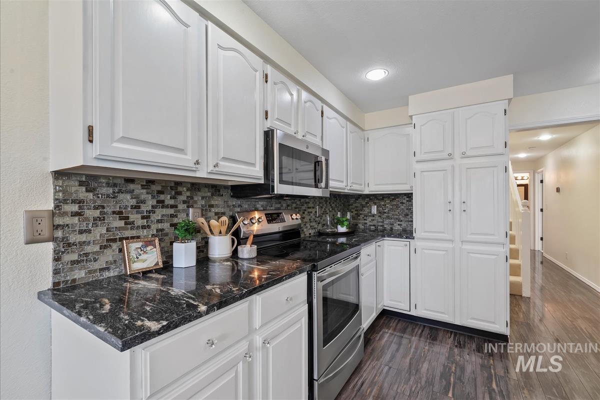 Kitchen featuring stainless steel appliances, dark wood-style floors, white cabinets, backsplash, and recessed lighting