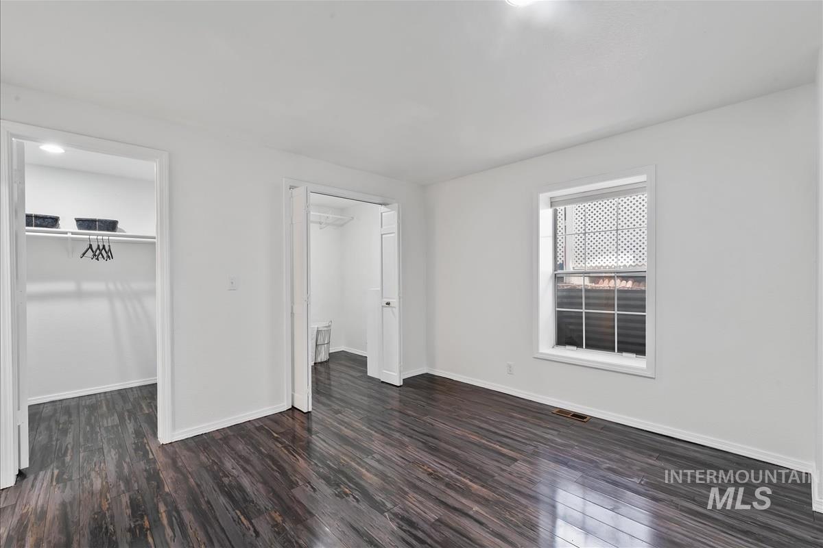 Unfurnished bedroom with a walk in closet, dark wood-style floors, and a closet