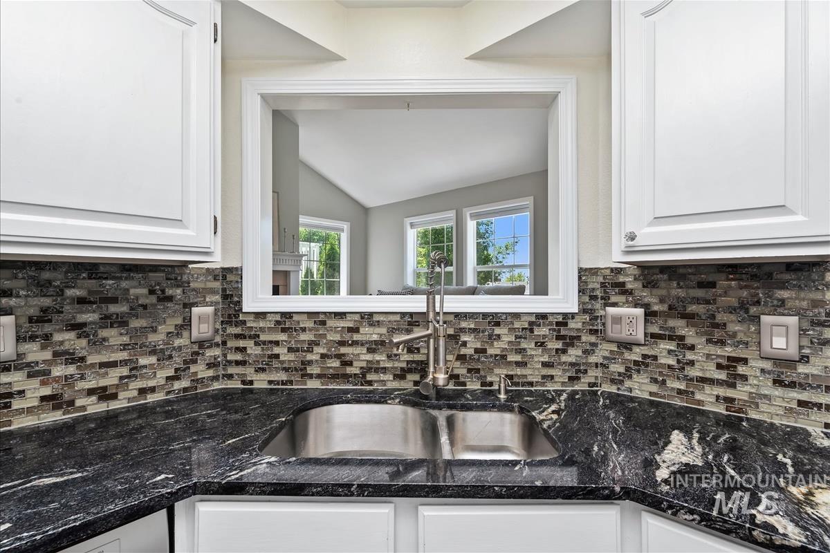 Kitchen with white cabinetry, backsplash, lofted ceiling, and dark stone countertops