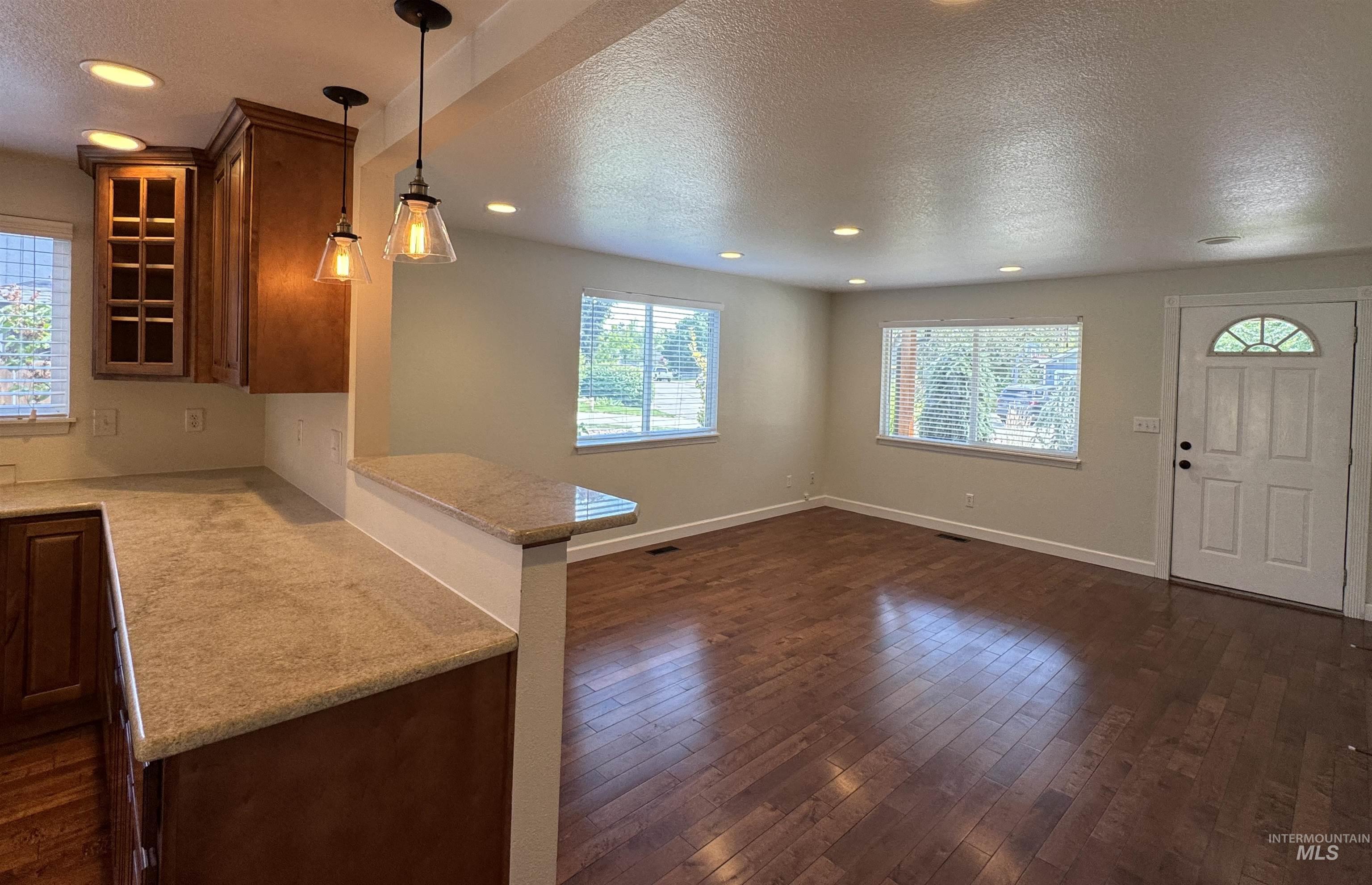 Kitchen with a textured ceiling, dark wood-style flooring, glass insert cabinets, recessed lighting, and a peninsula