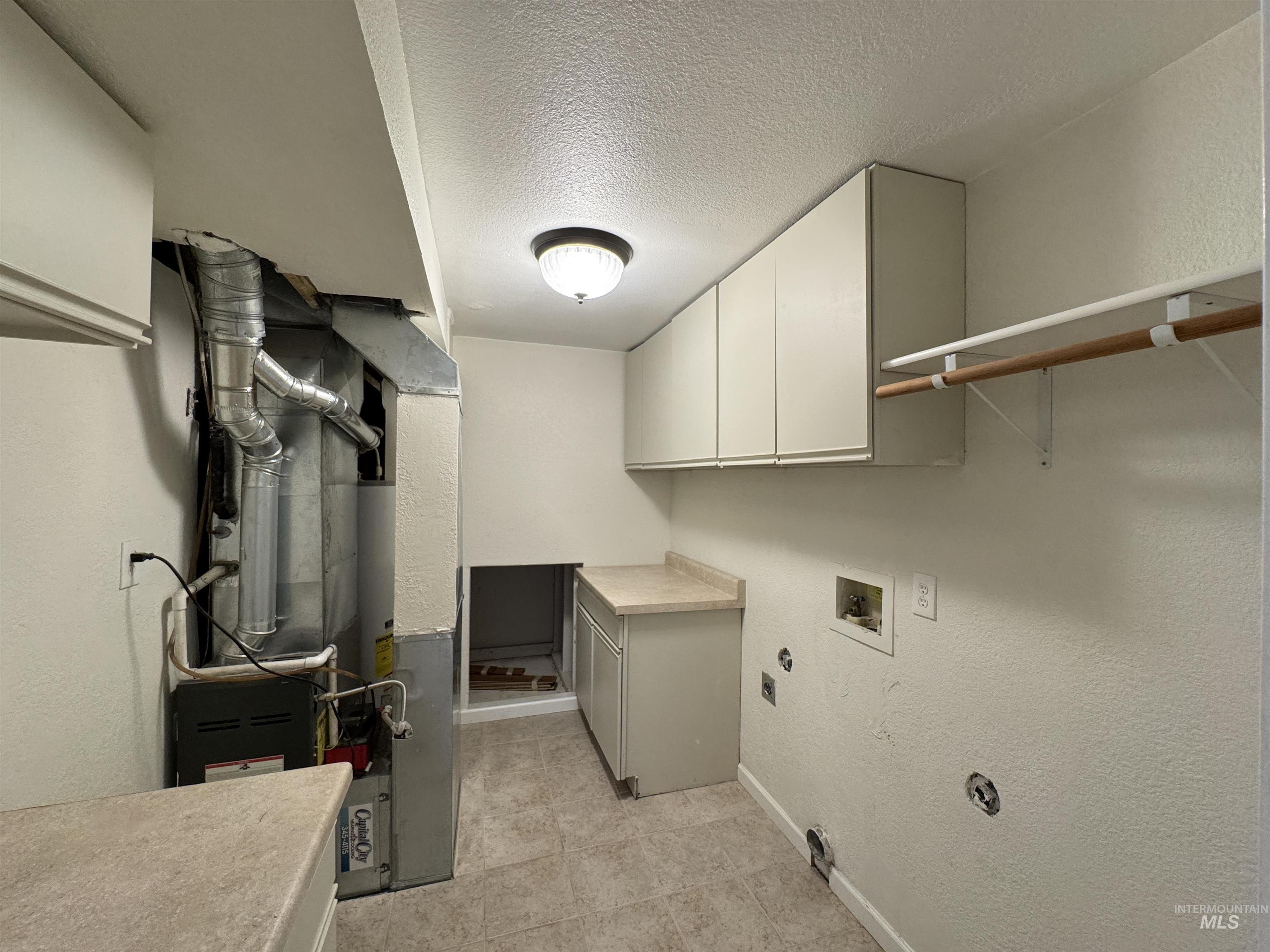 Laundry room featuring cabinet space, a textured ceiling, a textured wall, heating unit, and electric dryer hookup