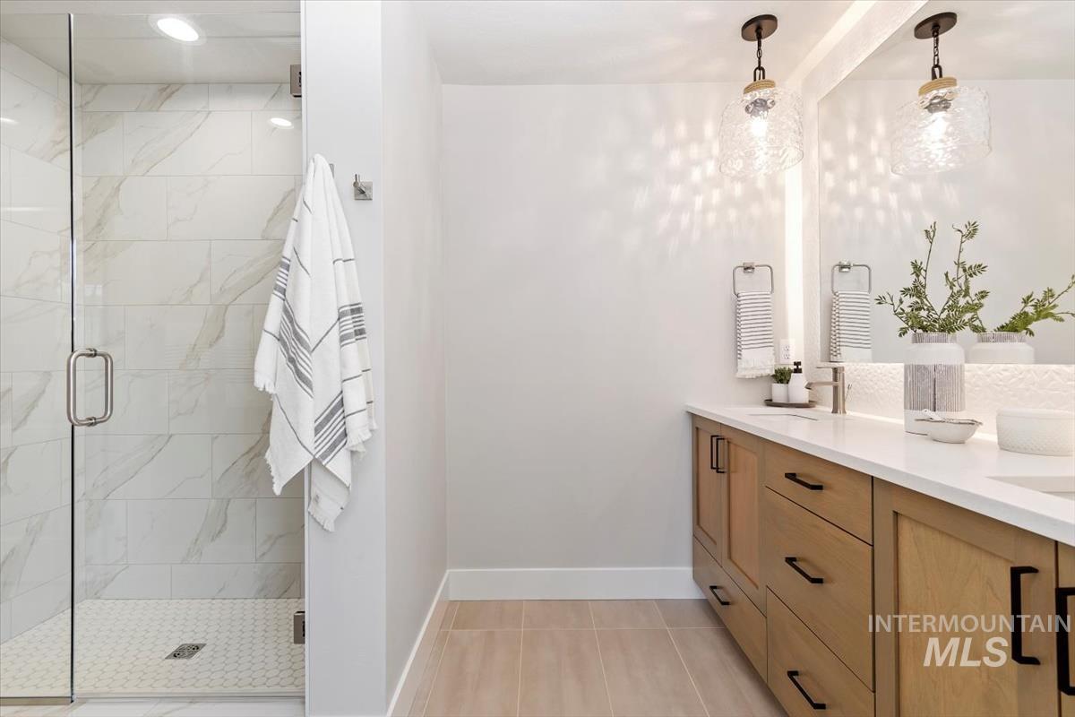 Bathroom featuring a marble finish shower, double vanity, and light tile patterned floors