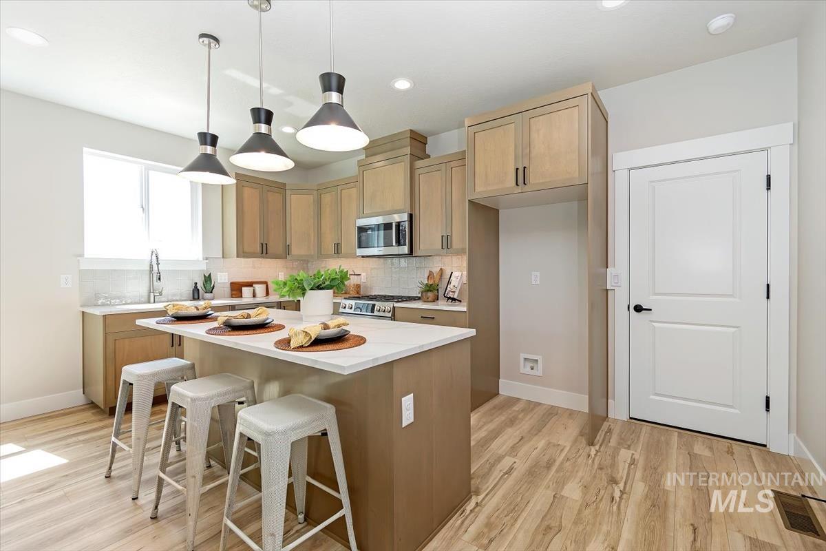 Kitchen featuring a breakfast bar area, decorative backsplash, pendant lighting, a center island, and recessed lighting