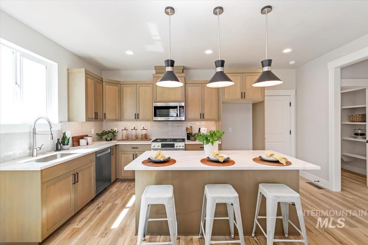 Kitchen featuring a breakfast bar, decorative light fixtures, stainless steel appliances, tasteful backsplash, and recessed lighting