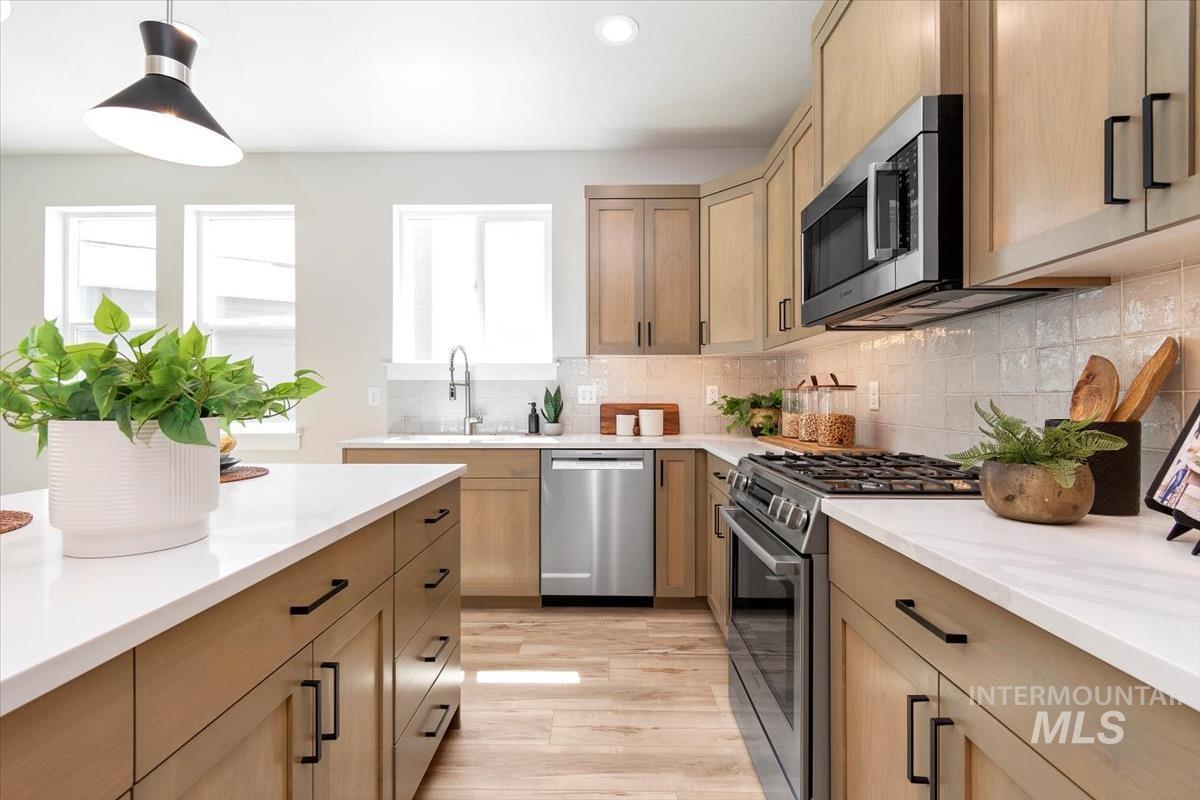 Kitchen featuring appliances with stainless steel finishes, pendant lighting, backsplash, light wood-style floors, and recessed lighting