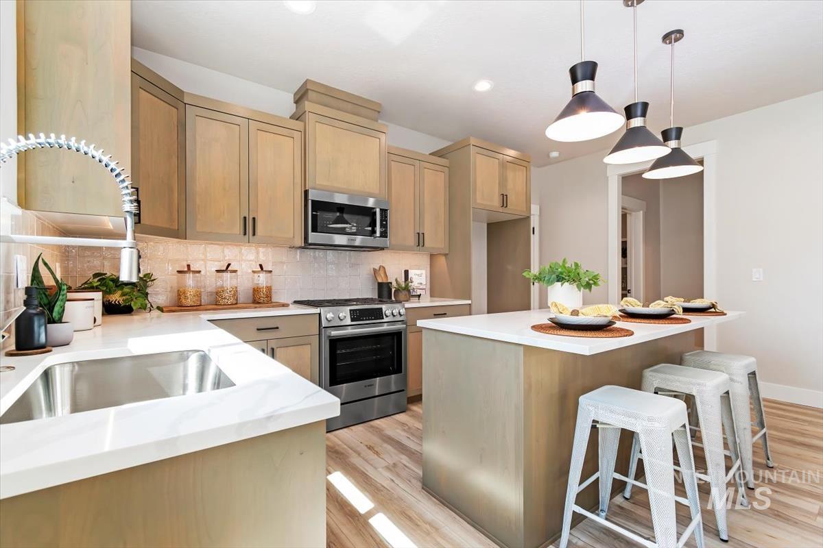 Kitchen with a kitchen bar, backsplash, appliances with stainless steel finishes, a kitchen island, and decorative light fixtures