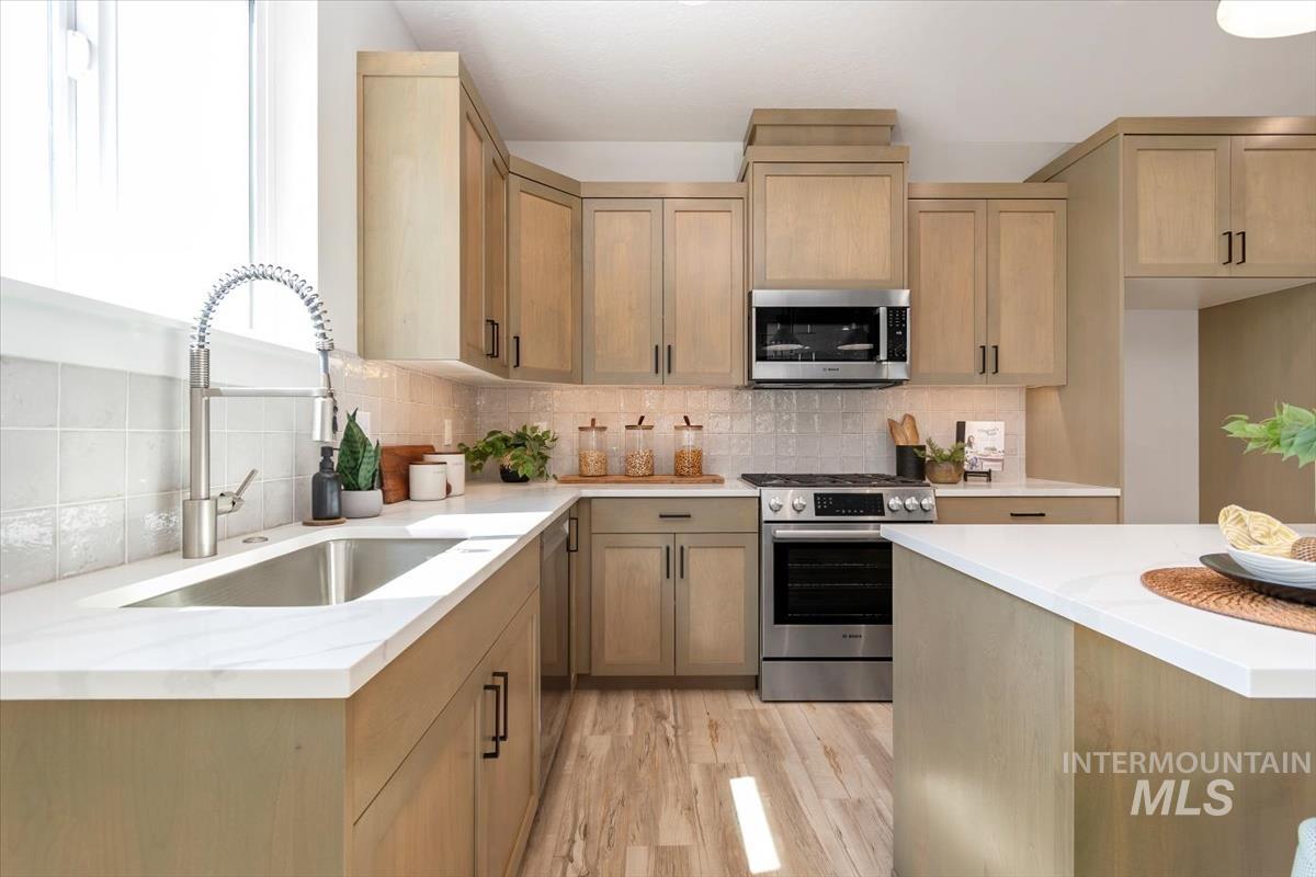 Kitchen with stainless steel appliances, decorative backsplash, light stone counters, light wood finished floors, and light brown cabinetry