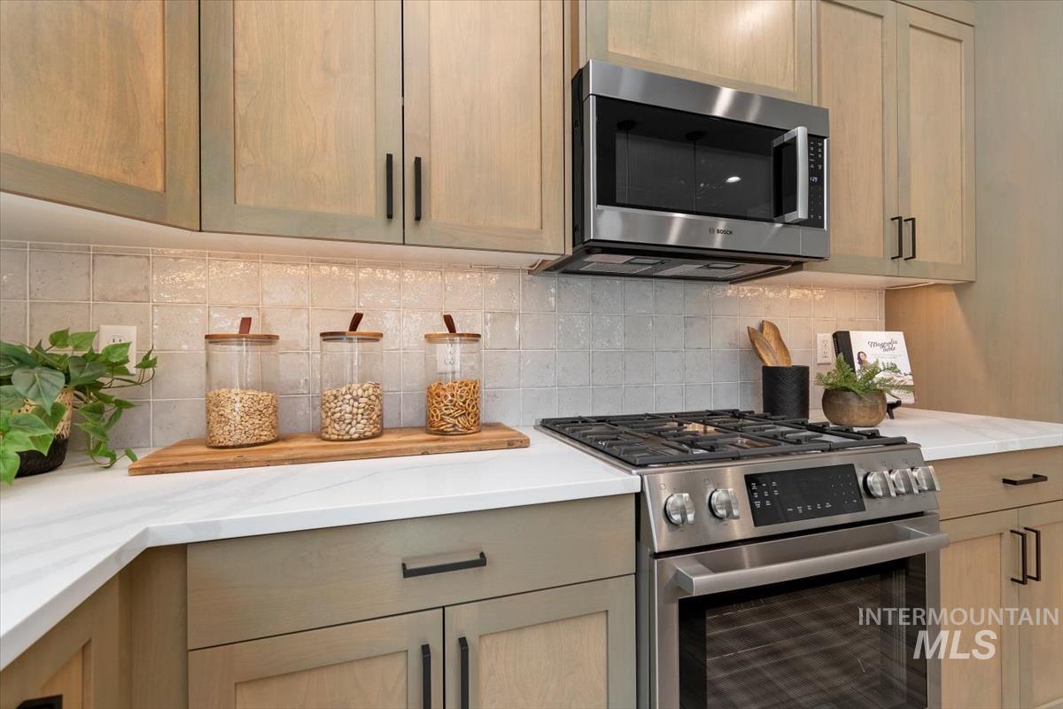 Kitchen with stainless steel appliances, backsplash, and light stone counters