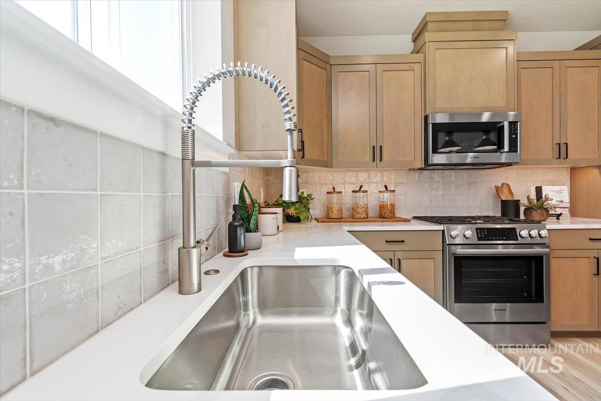 Kitchen featuring appliances with stainless steel finishes, decorative backsplash, and light stone countertops
