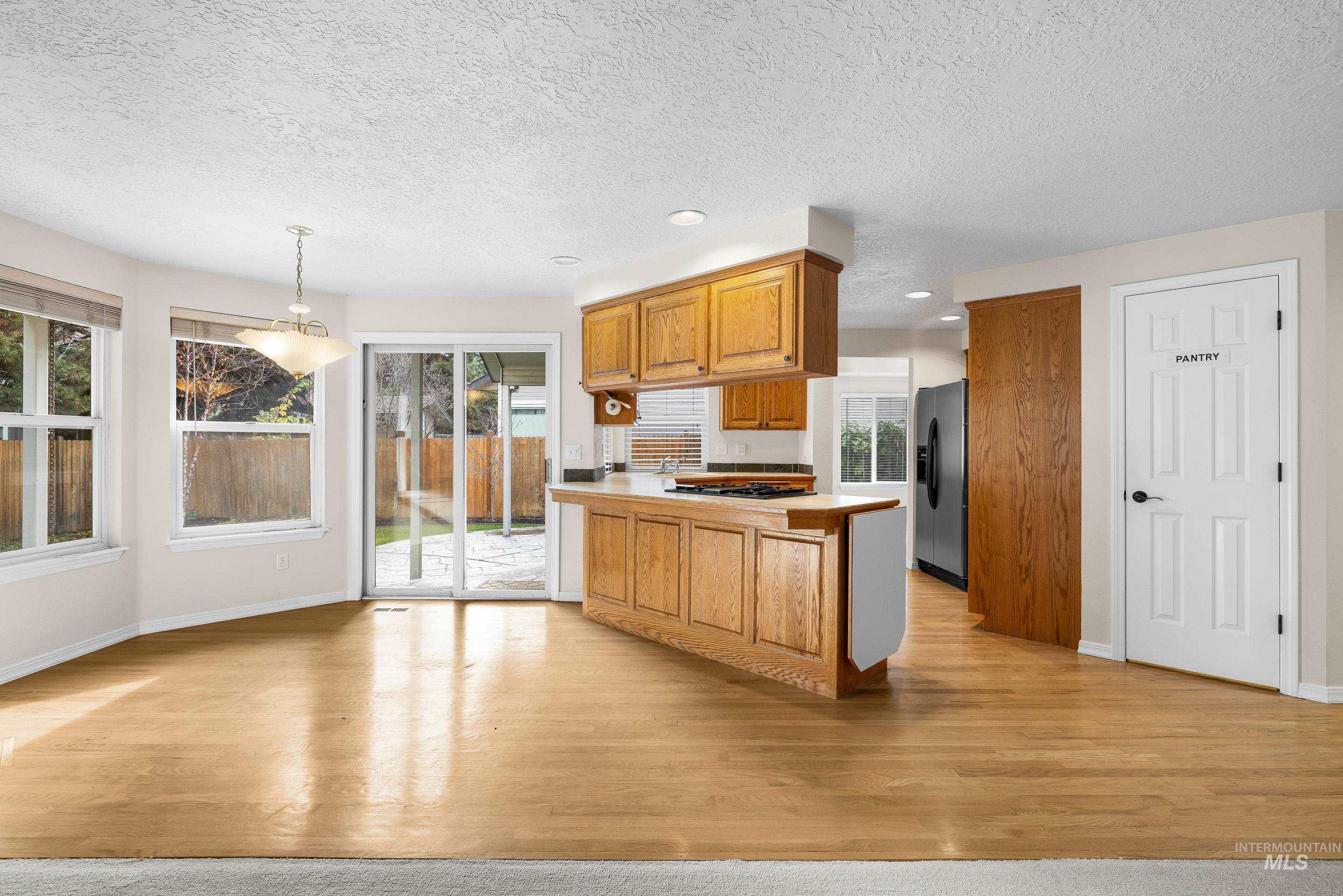 Kitchen with a peninsula, brown cabinets, pendant lighting, a textured ceiling, and recessed lighting