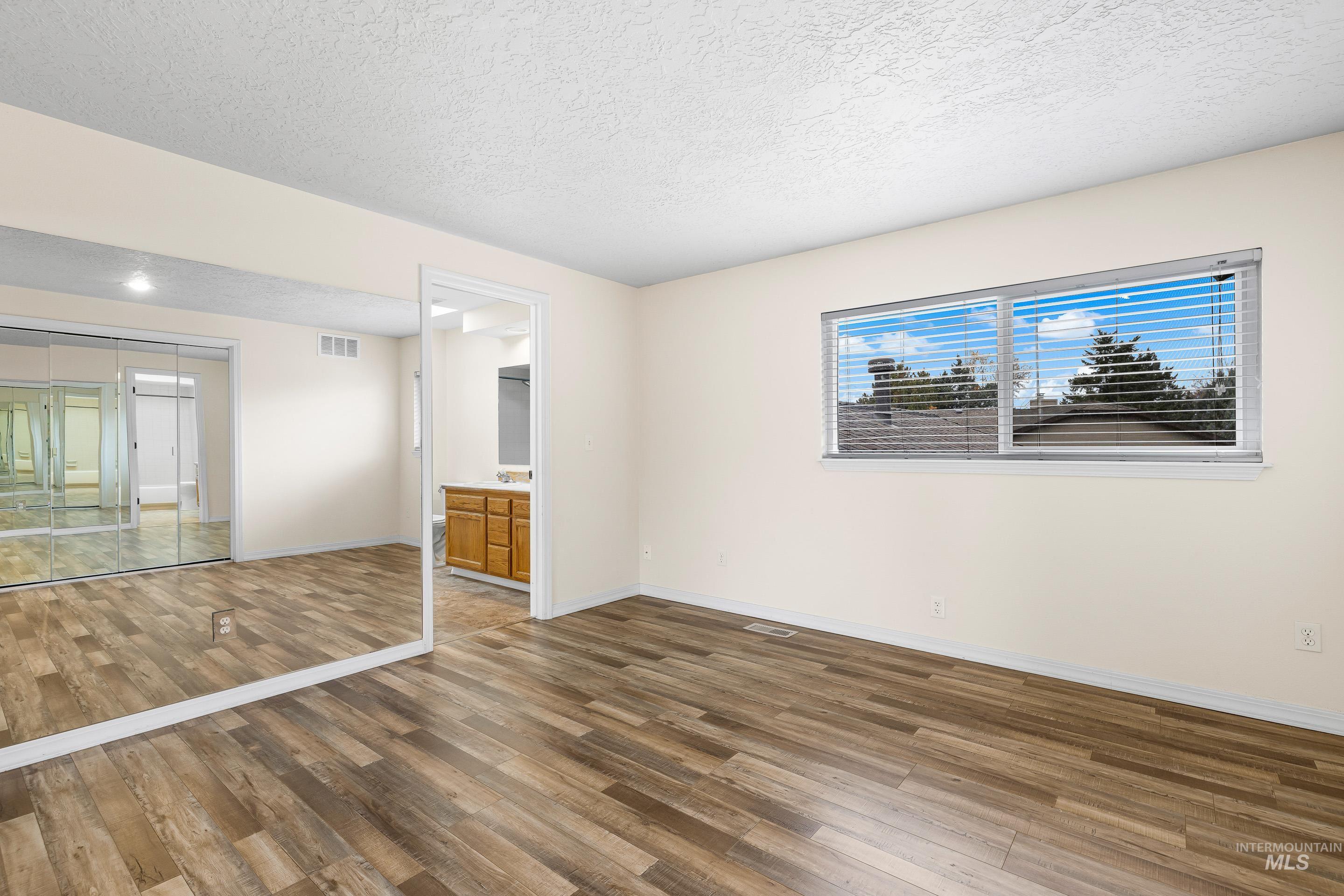 Unfurnished bedroom with hardwood / wood-style flooring, a closet, a textured ceiling, and ensuite bath
