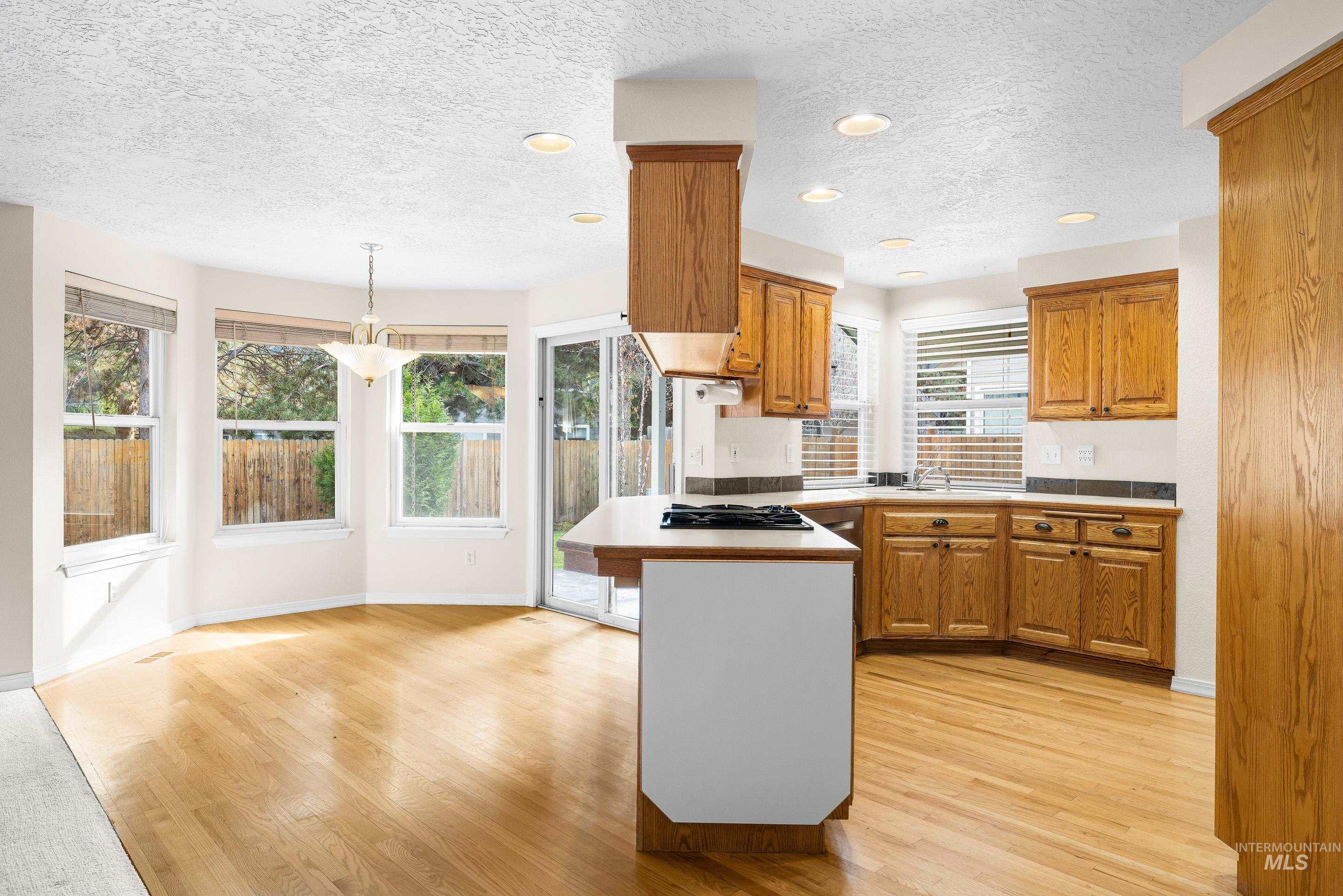 Kitchen with brown cabinets, a textured ceiling, a peninsula, hanging light fixtures, and light wood-style flooring