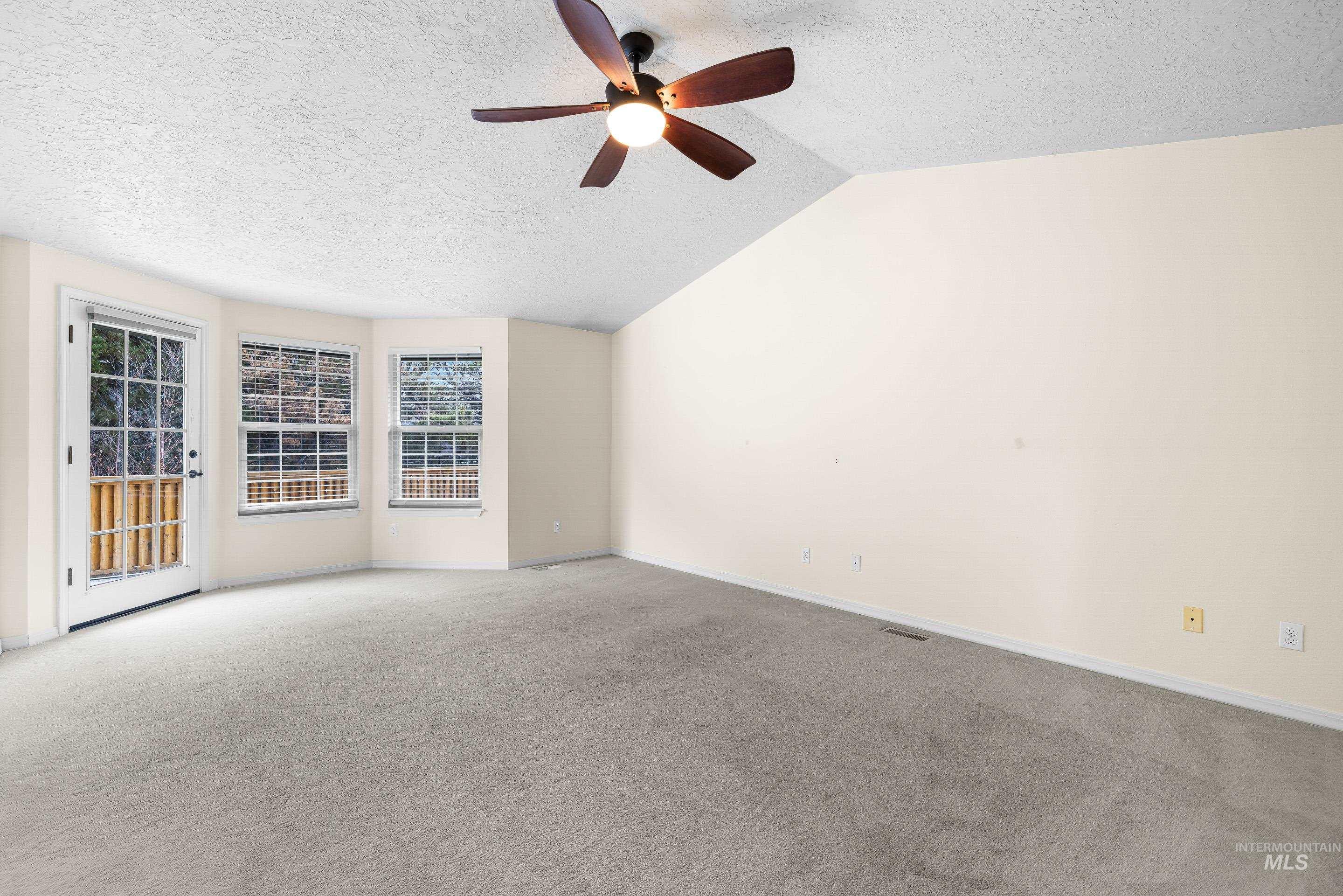 Spare room featuring a textured ceiling, light colored carpet, vaulted ceiling, and ceiling fan