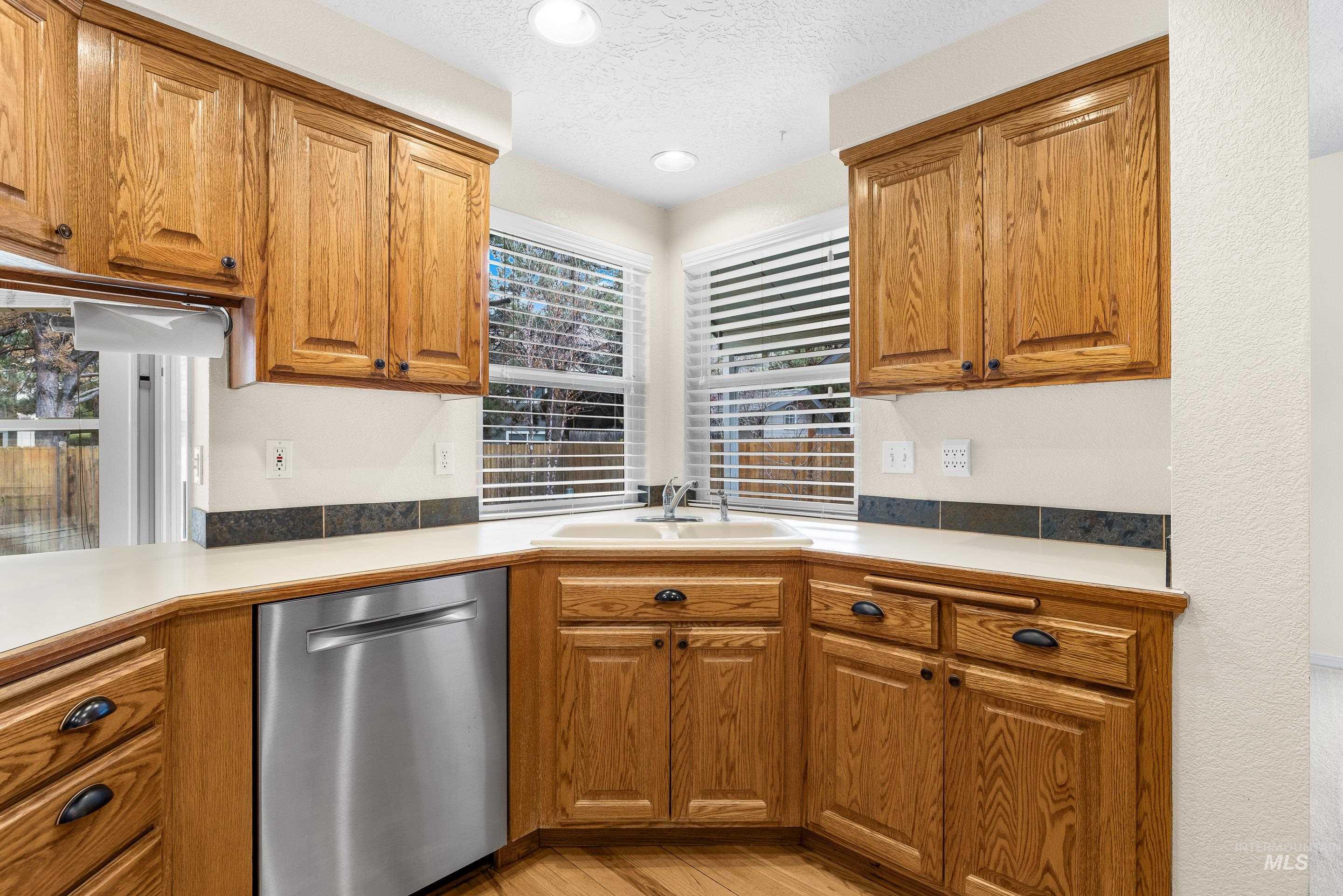 Kitchen with dishwasher, brown cabinetry, light countertops, a textured ceiling, and light wood-style flooring